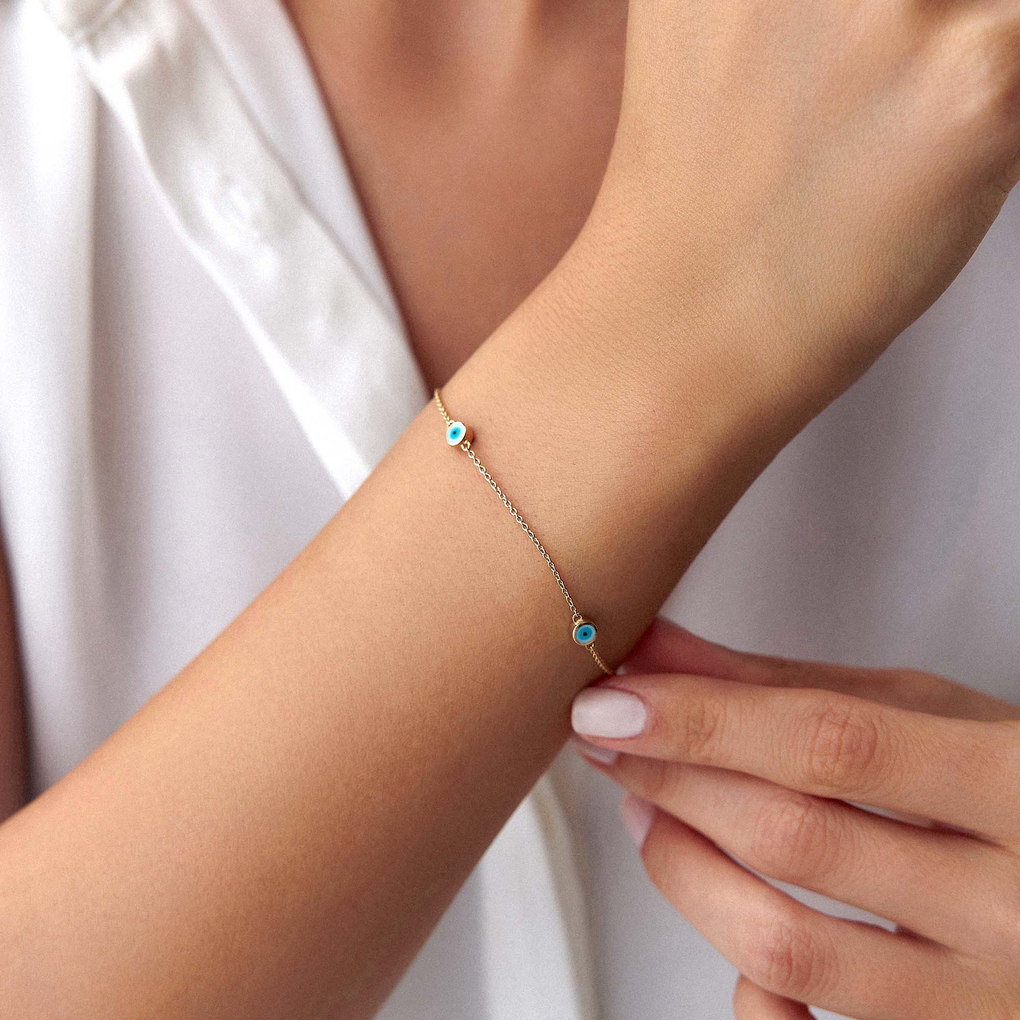 A 14 karat yellow gold bracelet with three white evil eye charms on a wrist
