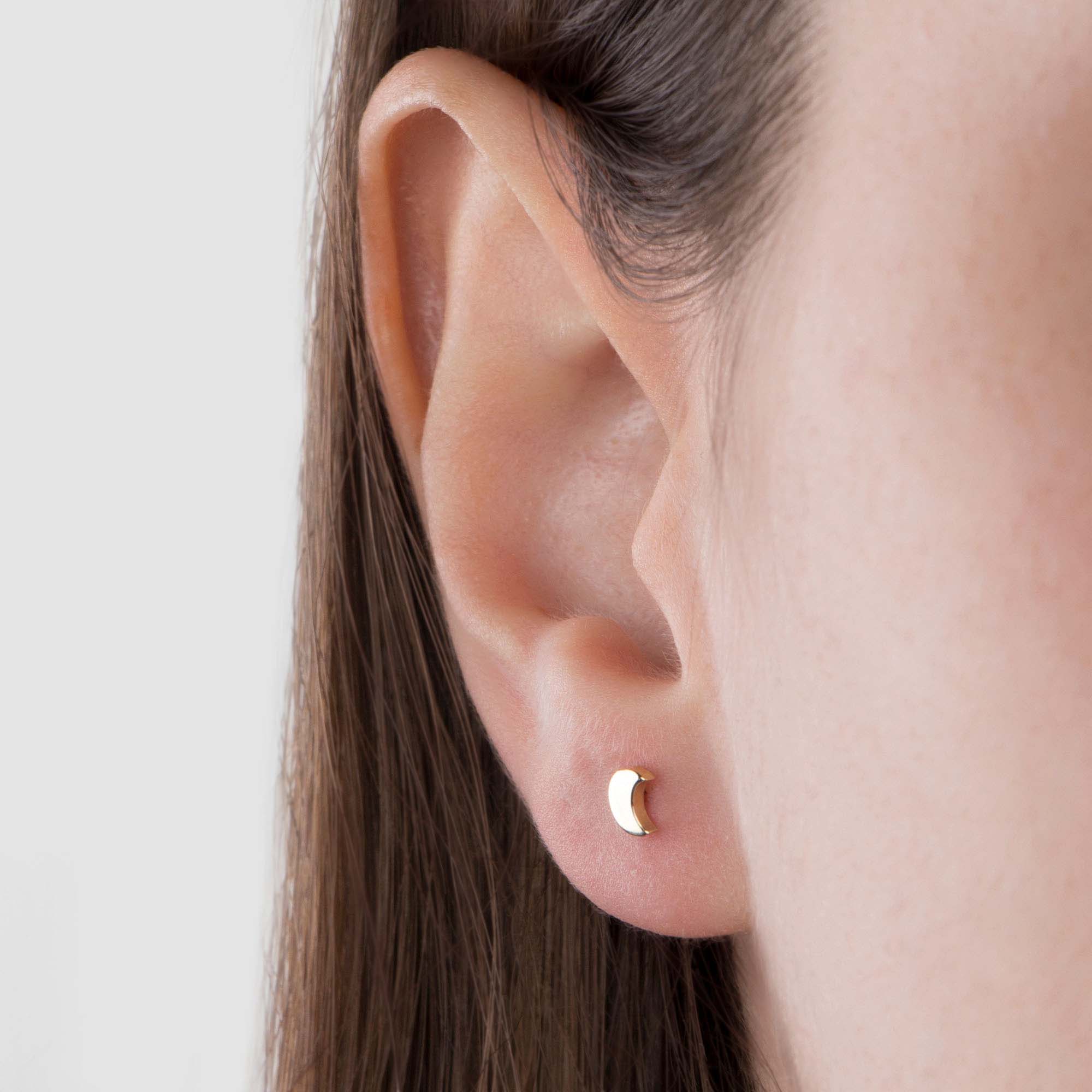 Close-up of an ear wearing a gold moon-shaped earring against a neutral background