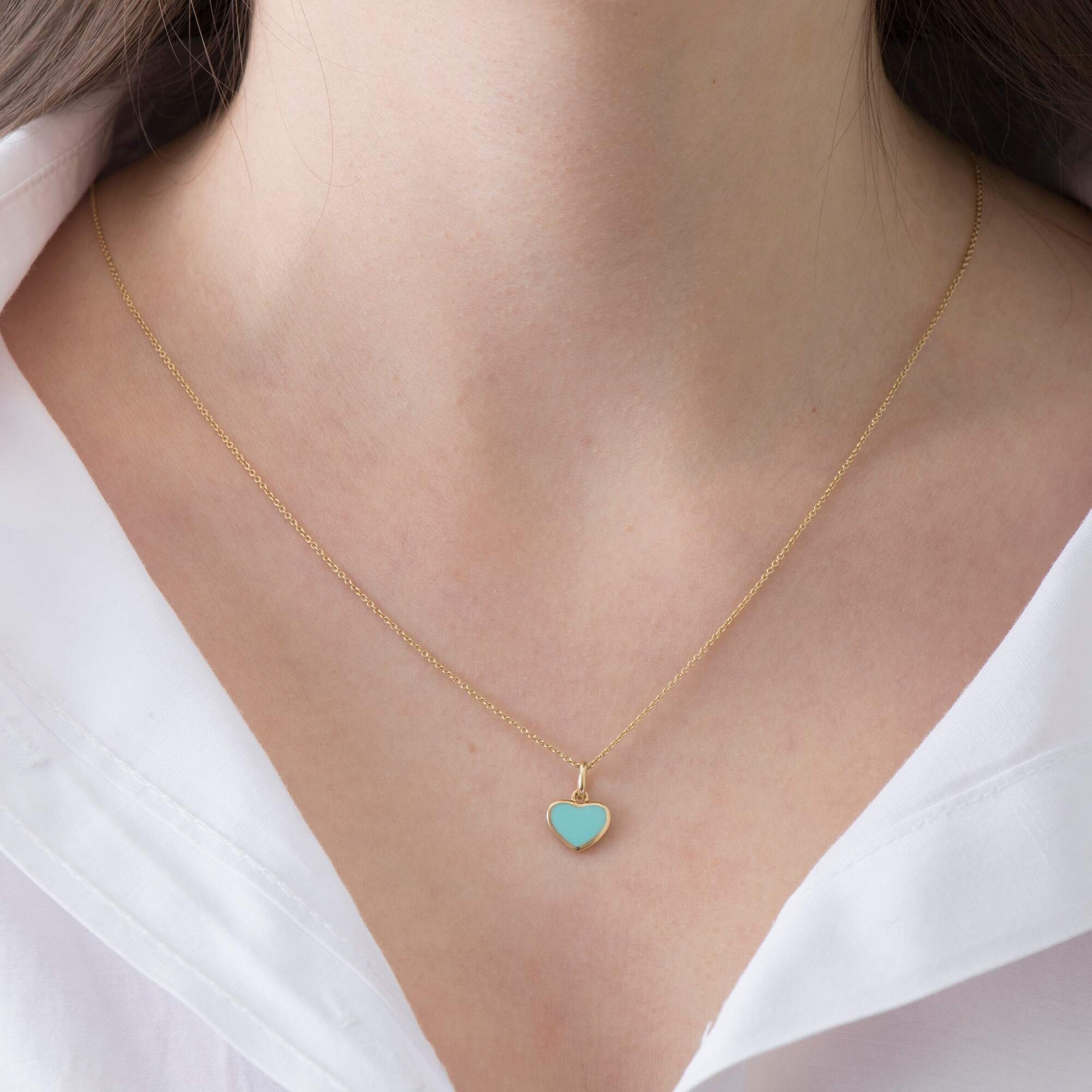 A model wearing a 14k yellow gold turquoise heart pendant on a thin gold chain.