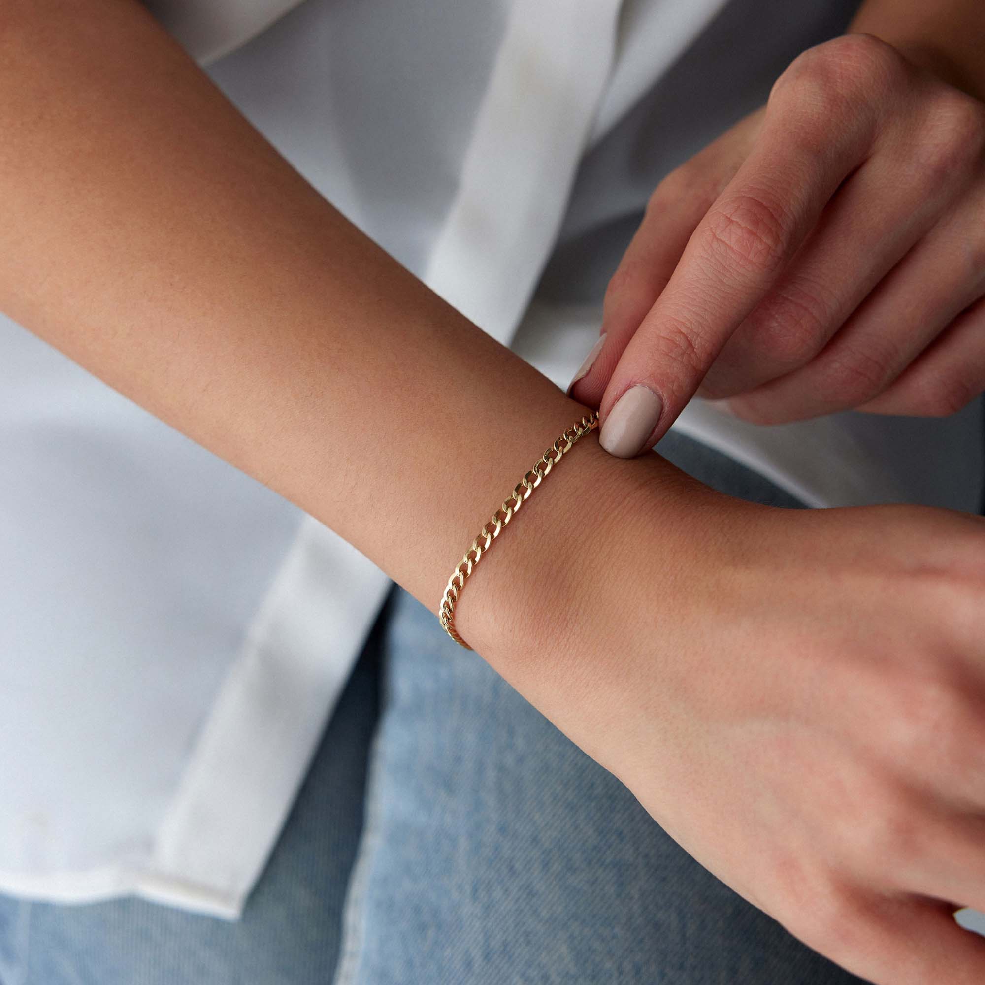 Gold curb bracelet on a wrist with a neutral background