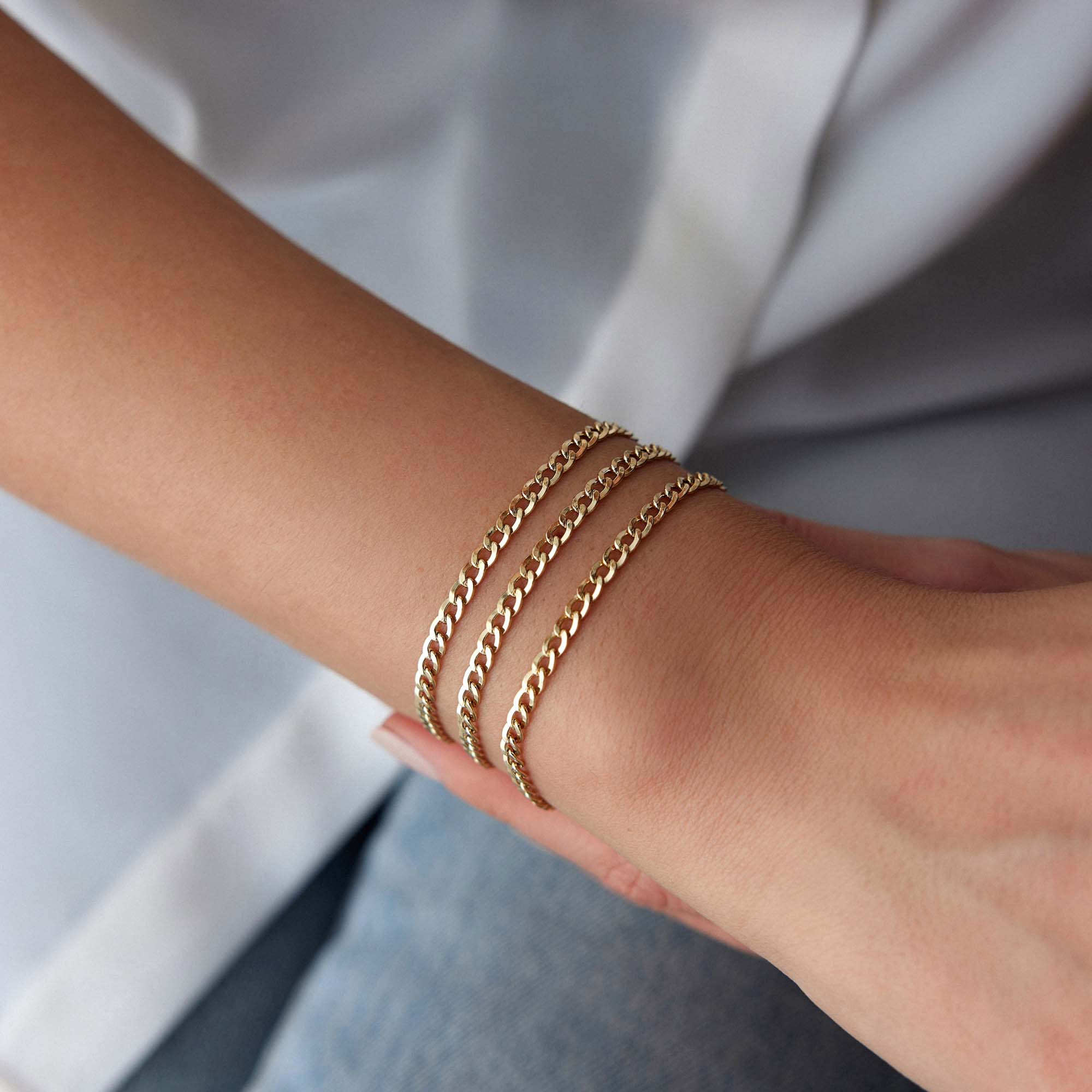 Minimal Gold curb chains bracelets on a person's wrist with a blurred background