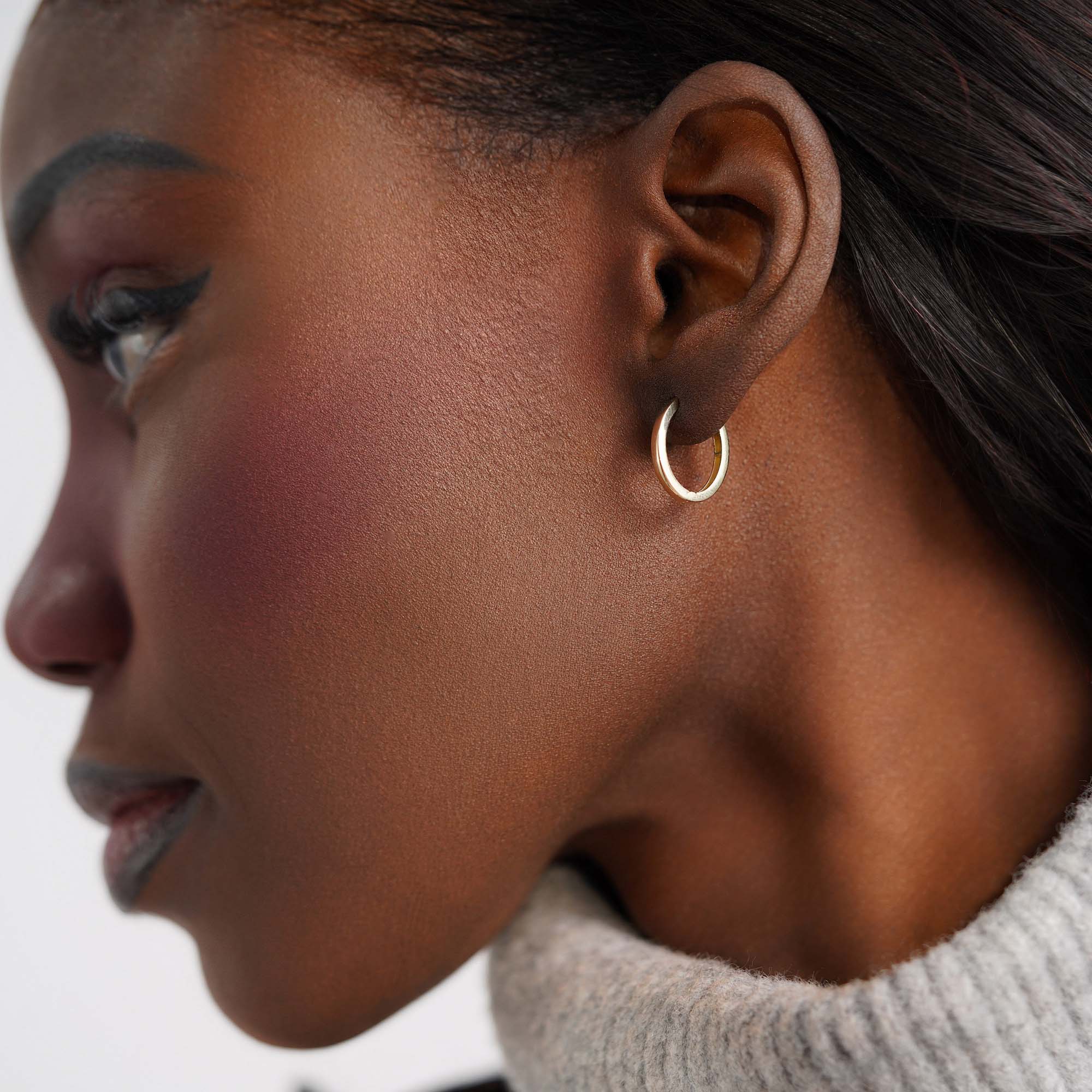 Close-up of a woman wearing an oval gold hoop earring against a neutral background