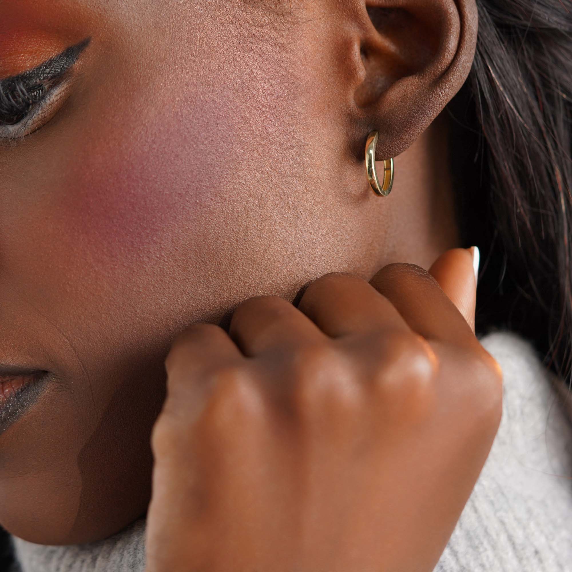 Close-up of a woman wearing an oval gold hoop earring against a neutral background