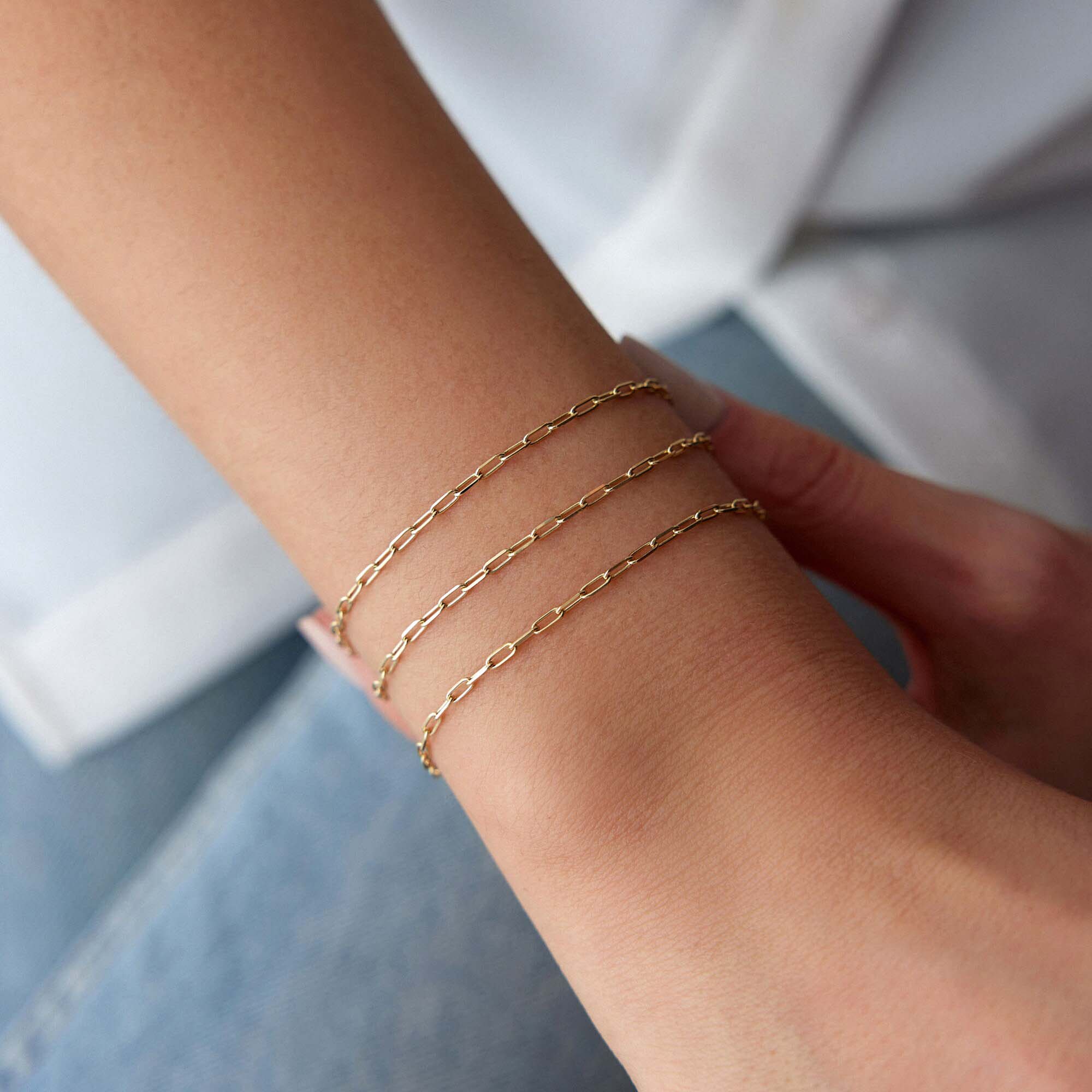 Minimal paperclip Gold chain bracelets on a wrist with a neutral background
