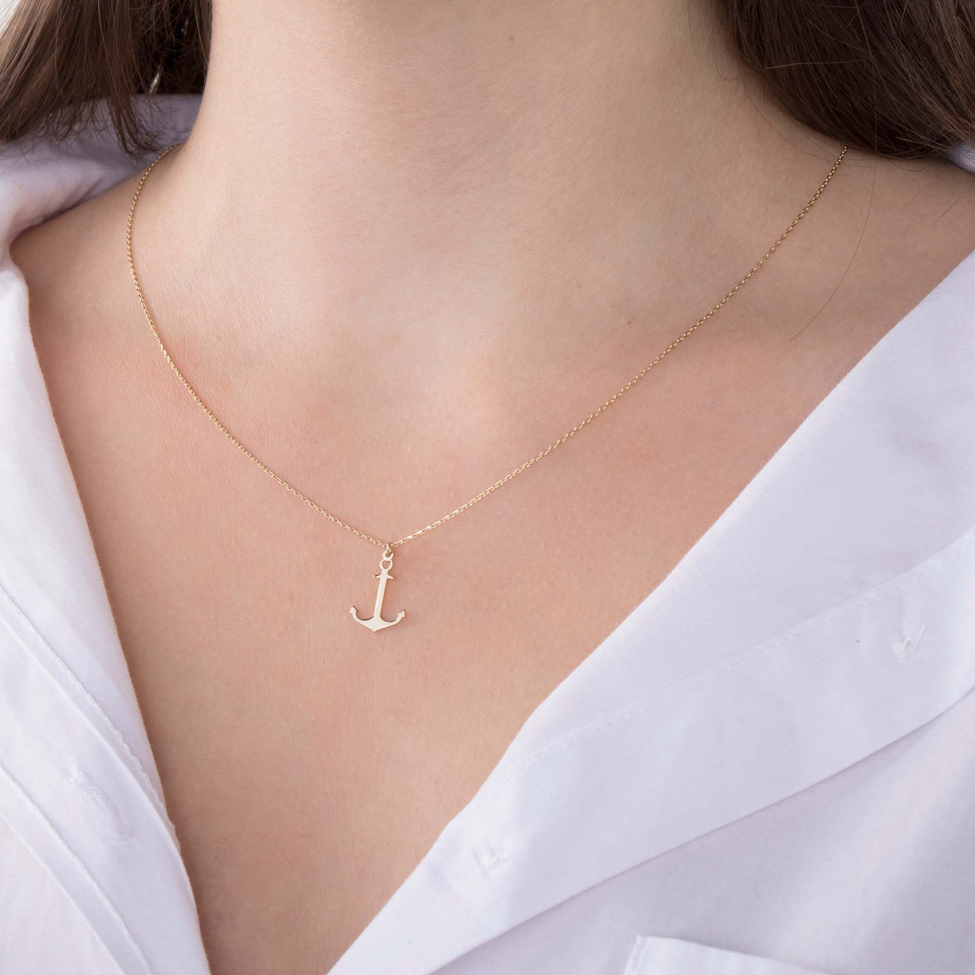 A minimal gold anchor necklace on a person's neck