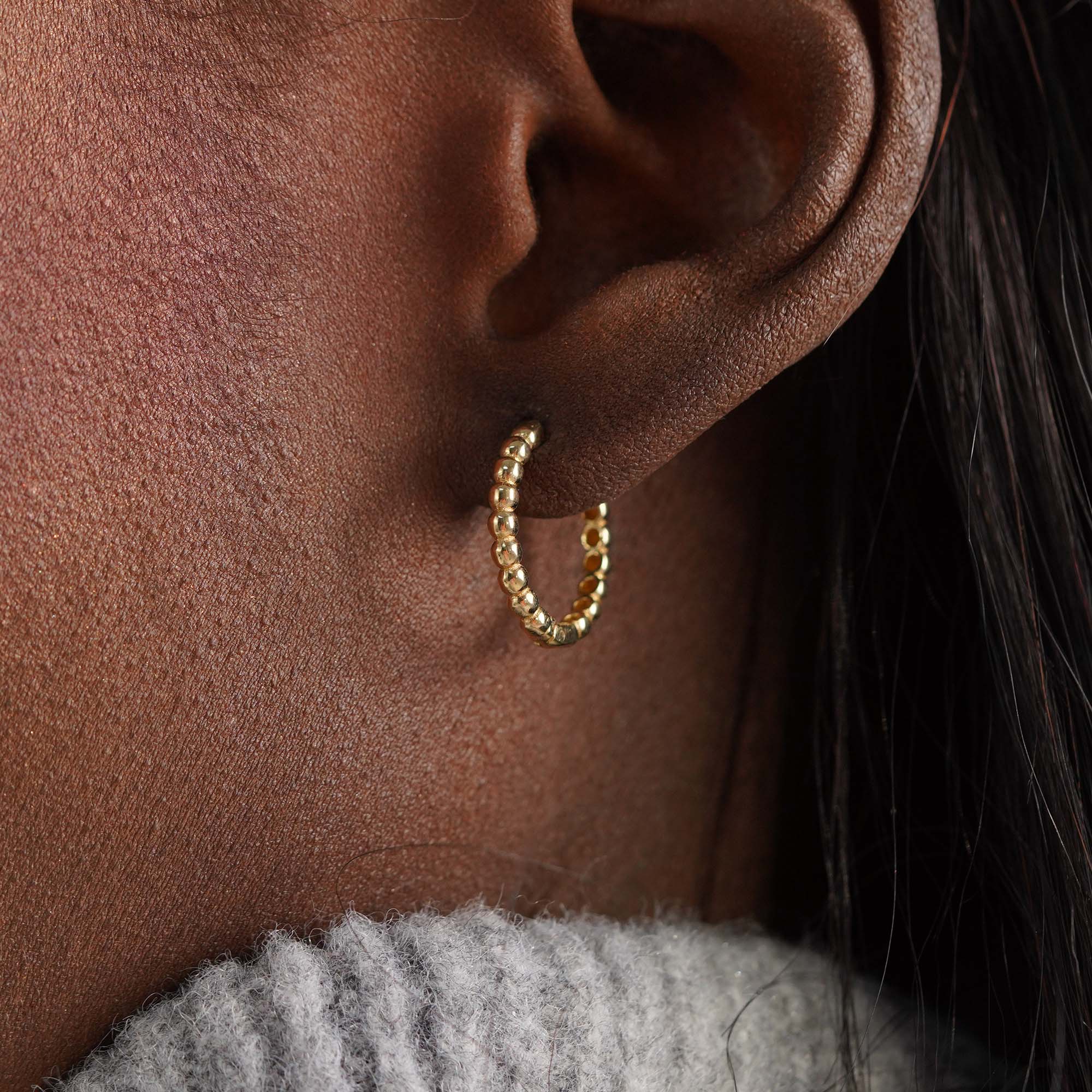 Close-up of an ear wearing a beaded gold hoop earring with a blurred background