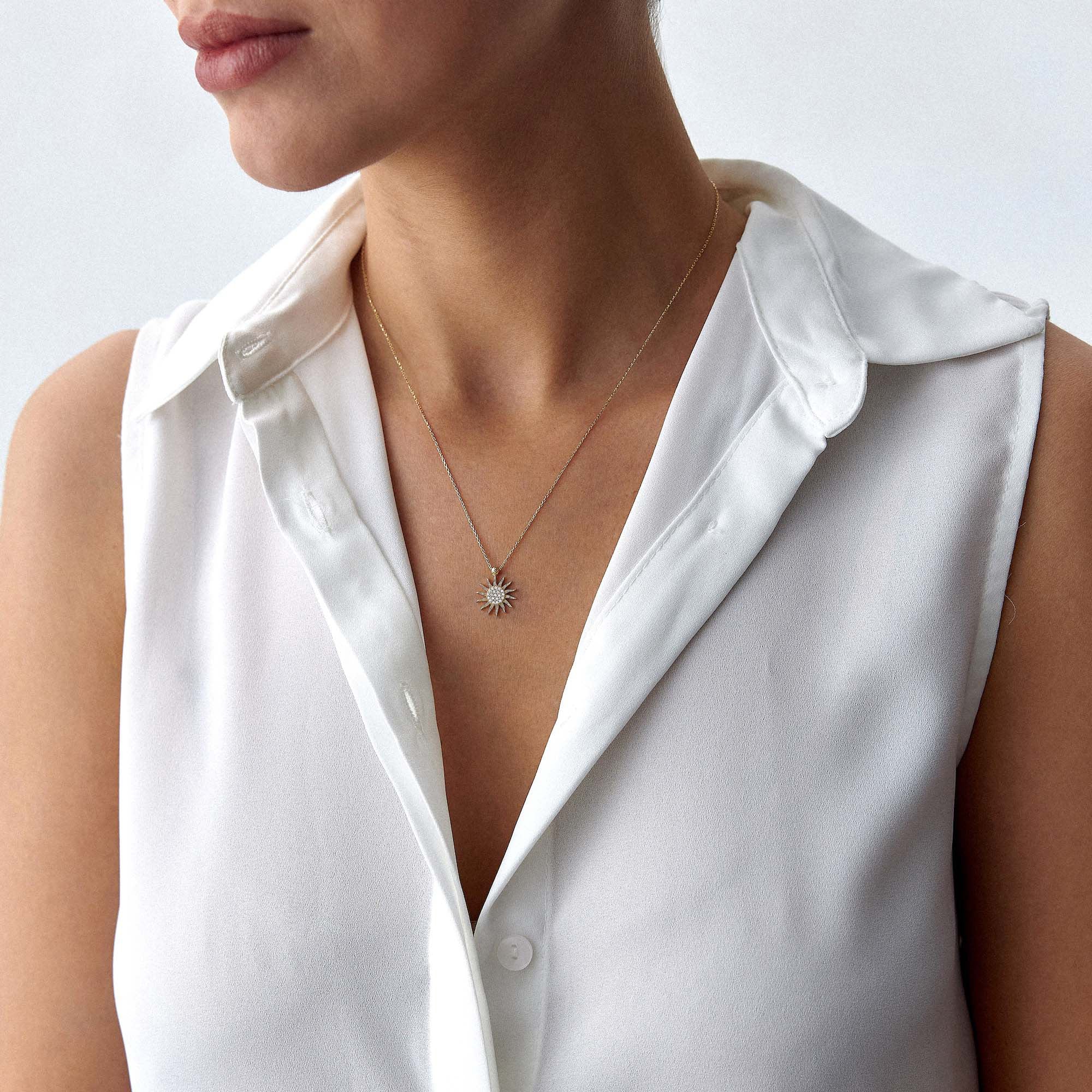 Person wearing a white sleeveless top with a necklace featuring a sun pendant.