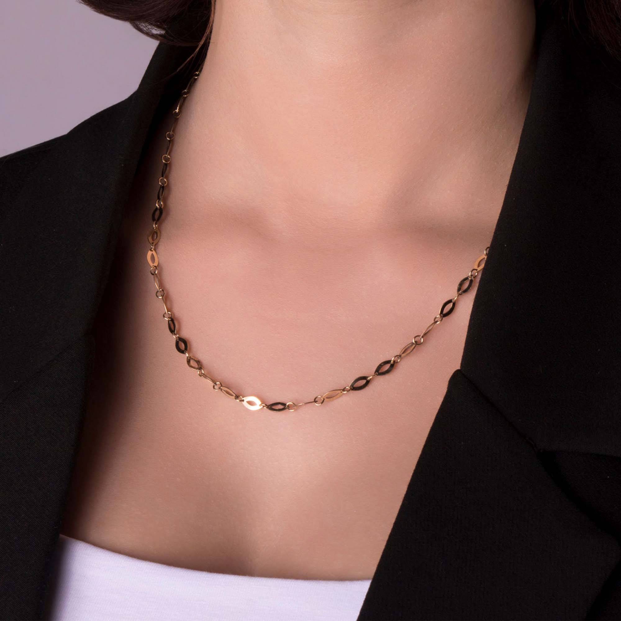 A 14k yellow gold oval mirror necklace shown on a person wearing a black blazer and white shirt against a purple background