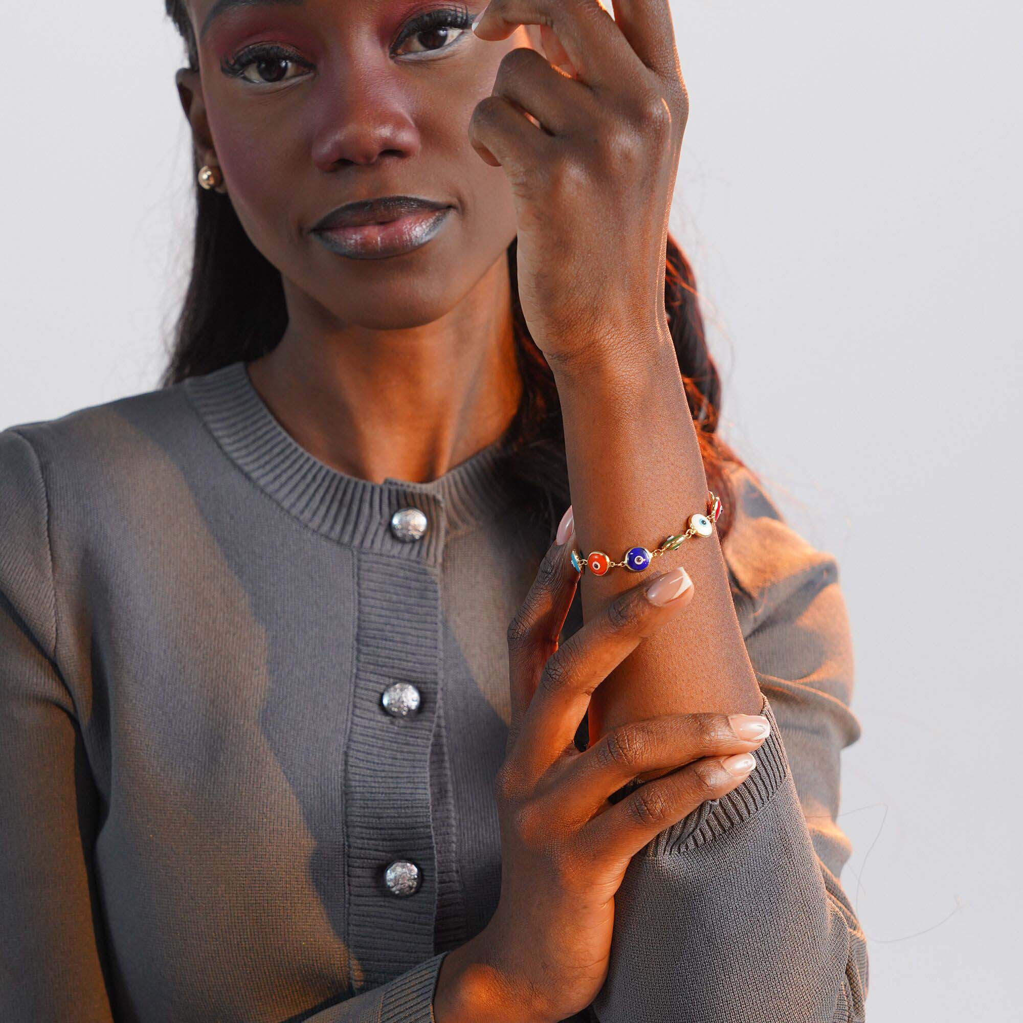 Woman wearing a gray cardigan with visible buttons, holding her wrist with an evil eye bracelet.