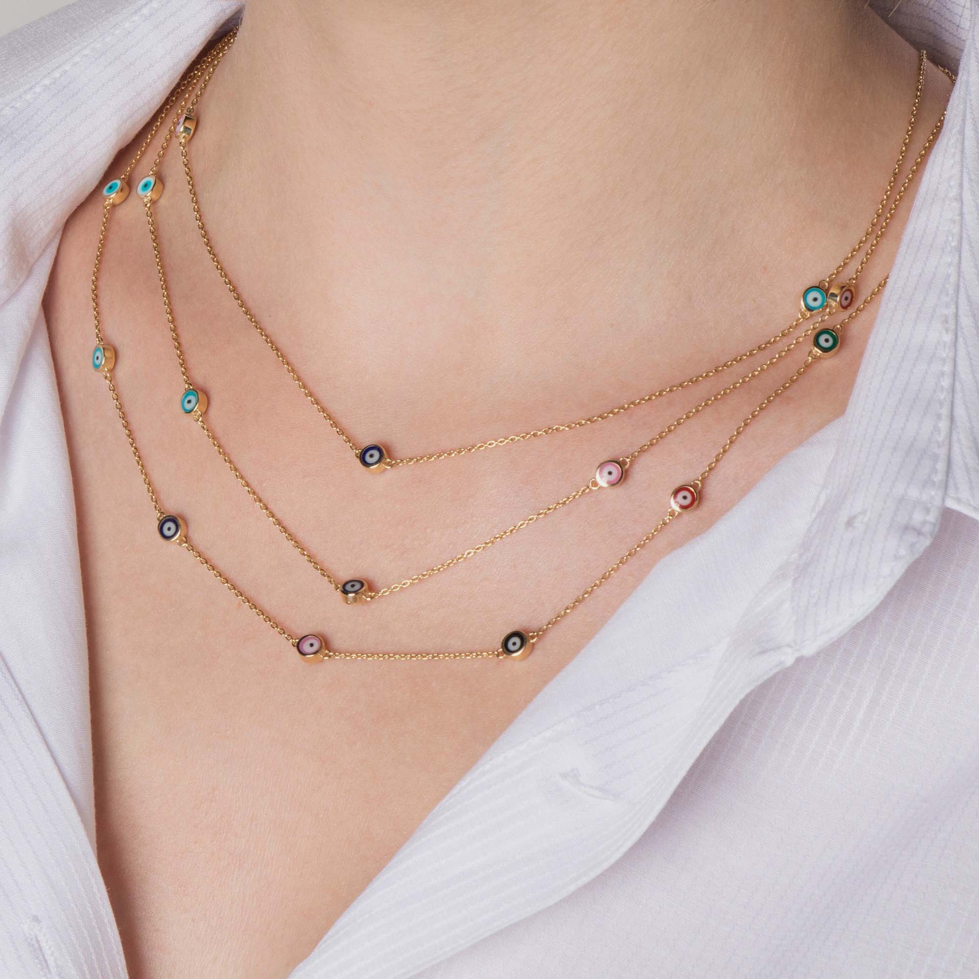 Close up of a model wearing 3 evil eye station necklaces. The first necklace features 3 multicolor evil eyes, the second necklace features 5 multicolor evil eyes, the third necklace features 7 multicolor evil eyes.