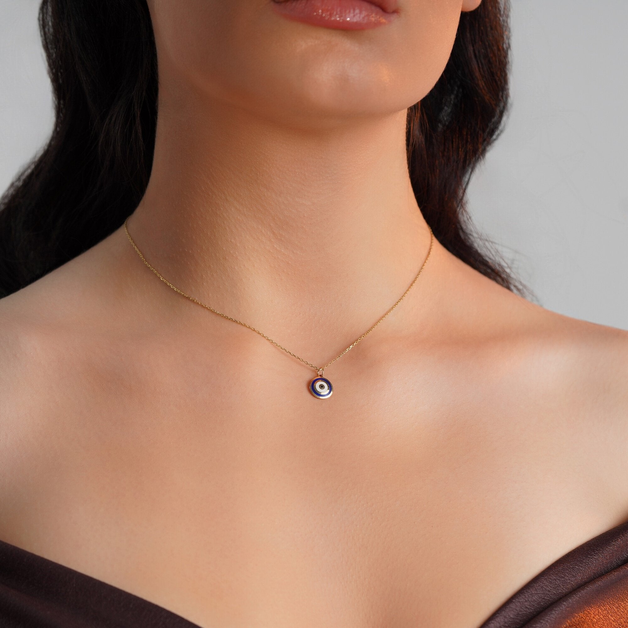 A navy blue evil eye pendant necklace in 14K gold displayed on a person's neck.