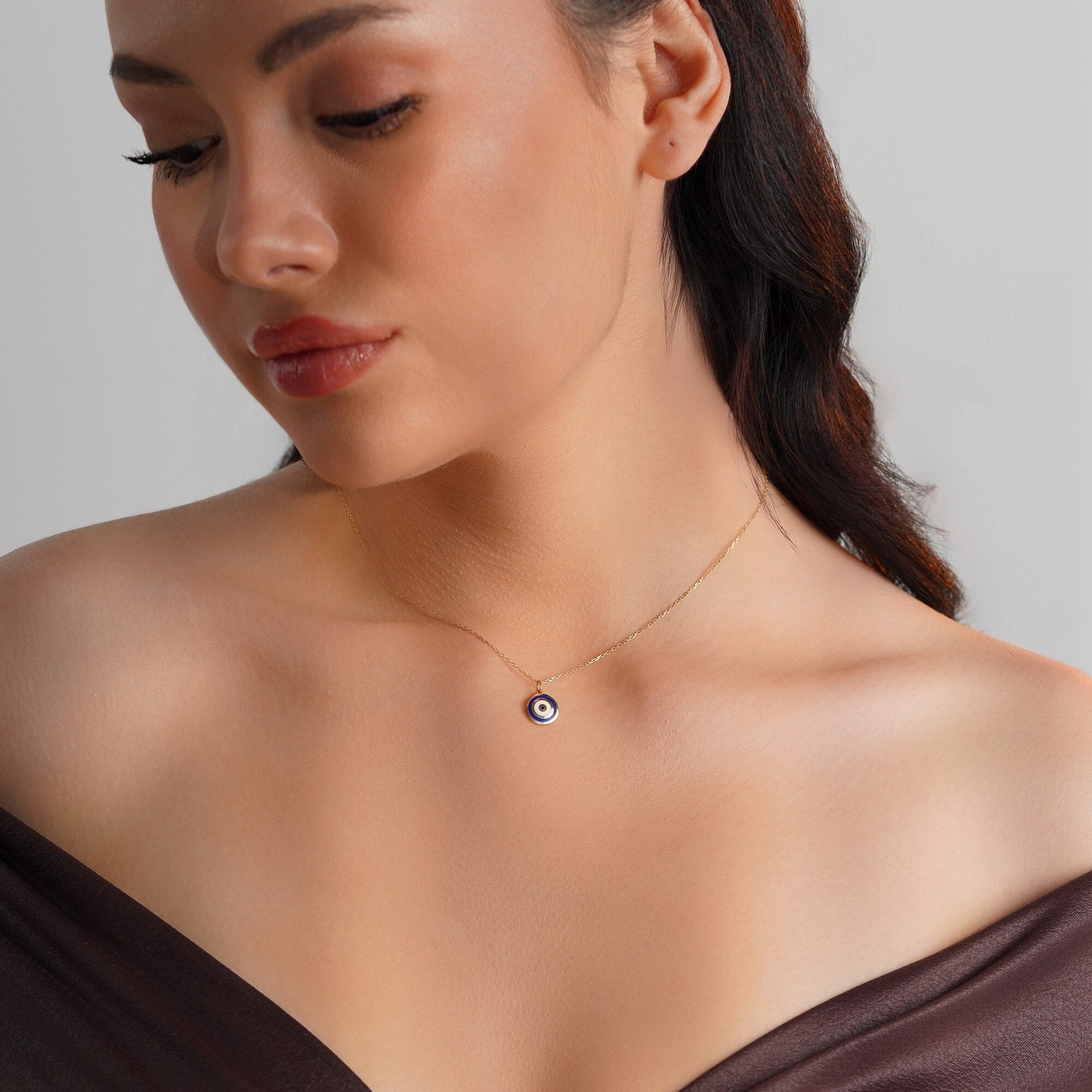 A navy blue evil eye pendant necklace in 14K gold displayed on a person's neck.