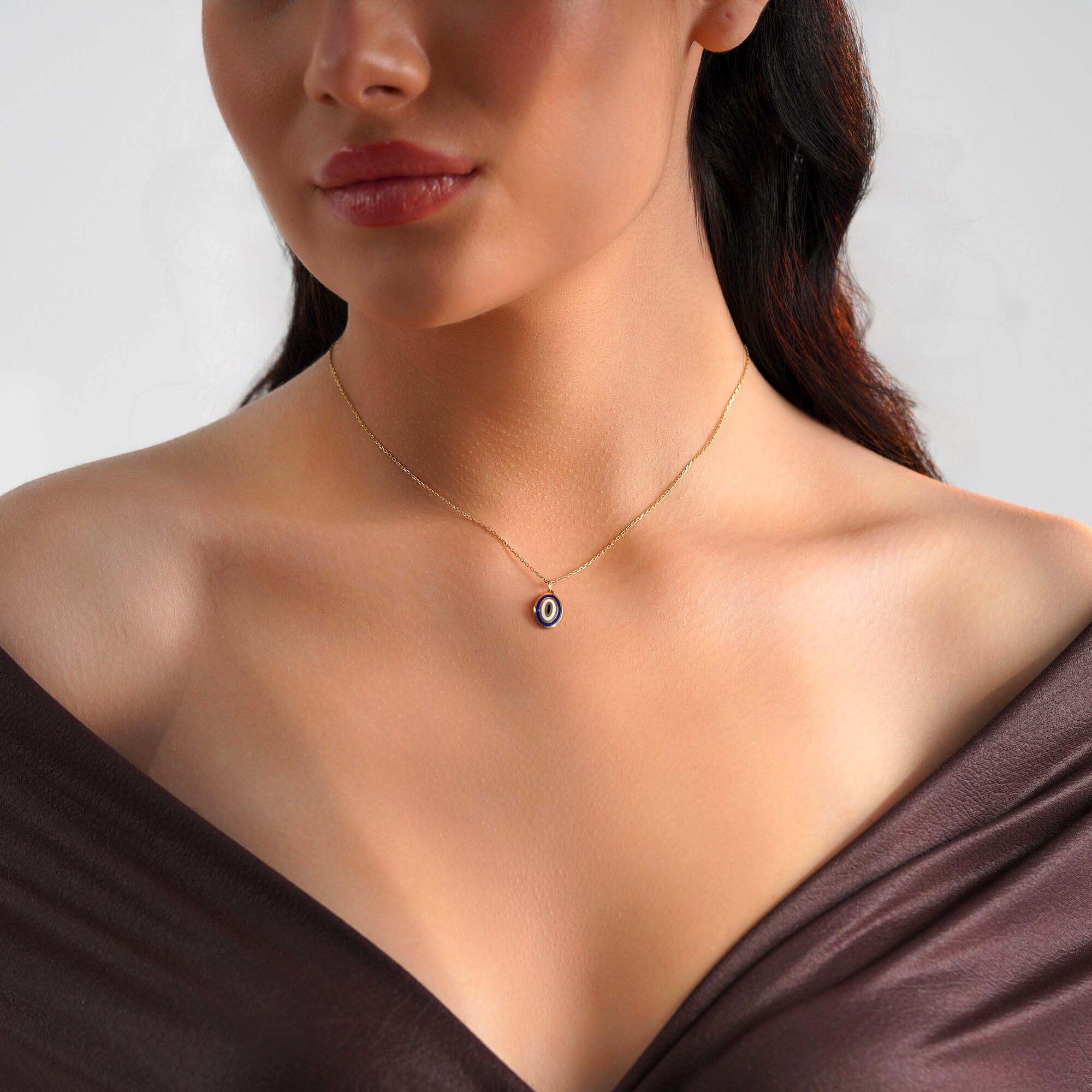 A model wearing an oval shaped 14k yellow gold evil eye pendant on a thin gold chain.