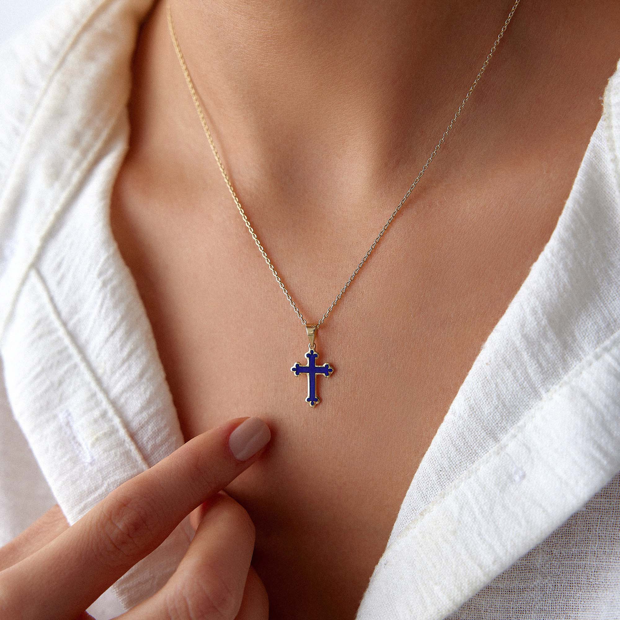 A 14k yellow gold small navy blue cross pendant worn on a thin gold chain.