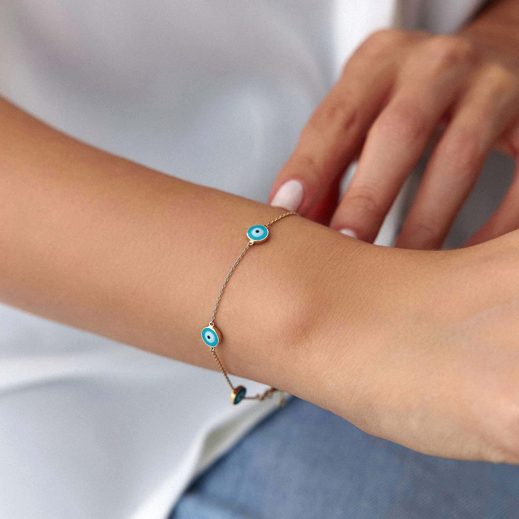 Close-up of a wrist wearing a bracelet with blue evil eyes on a plain background
