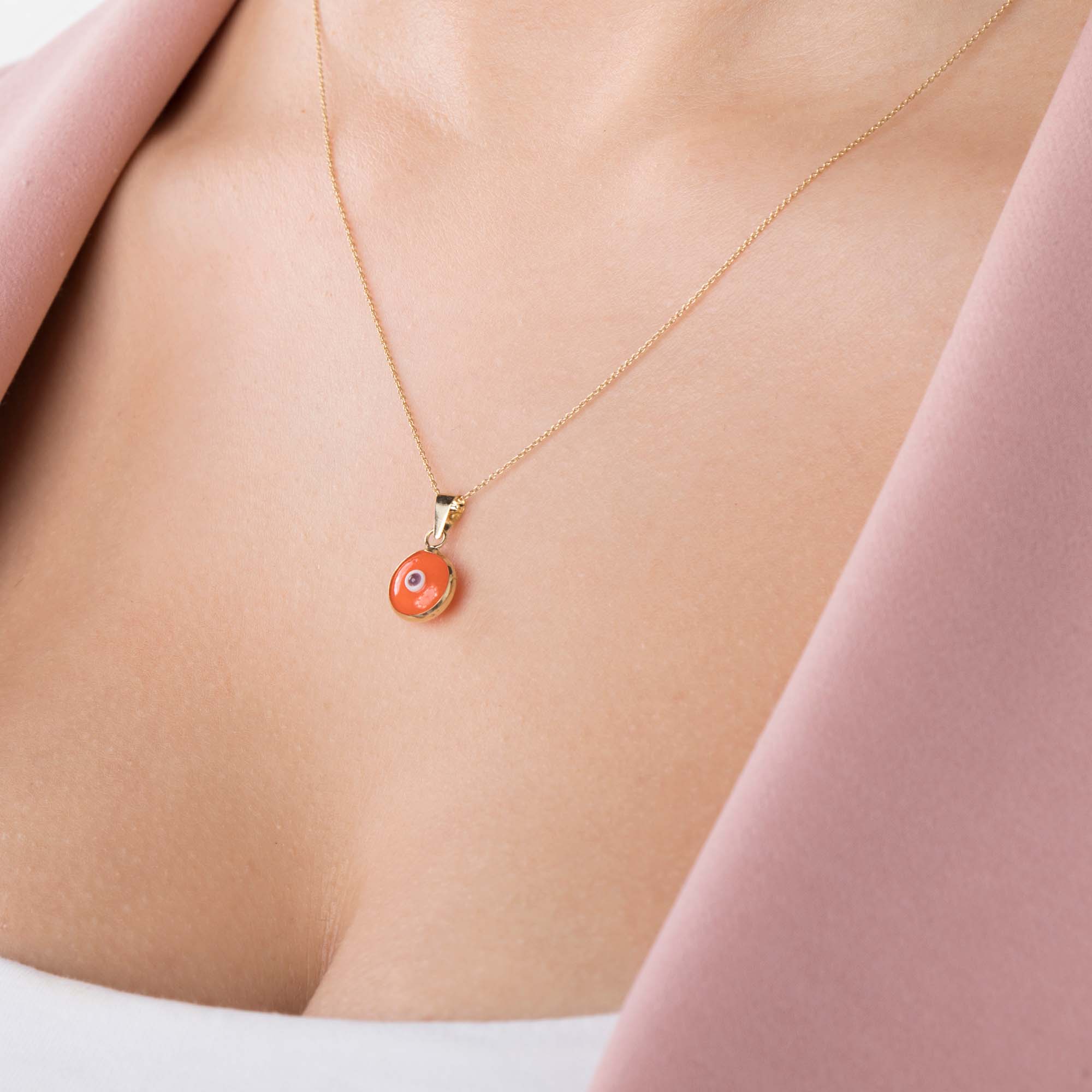 A model wearing an orange evil eye pendant on a thin gold chain