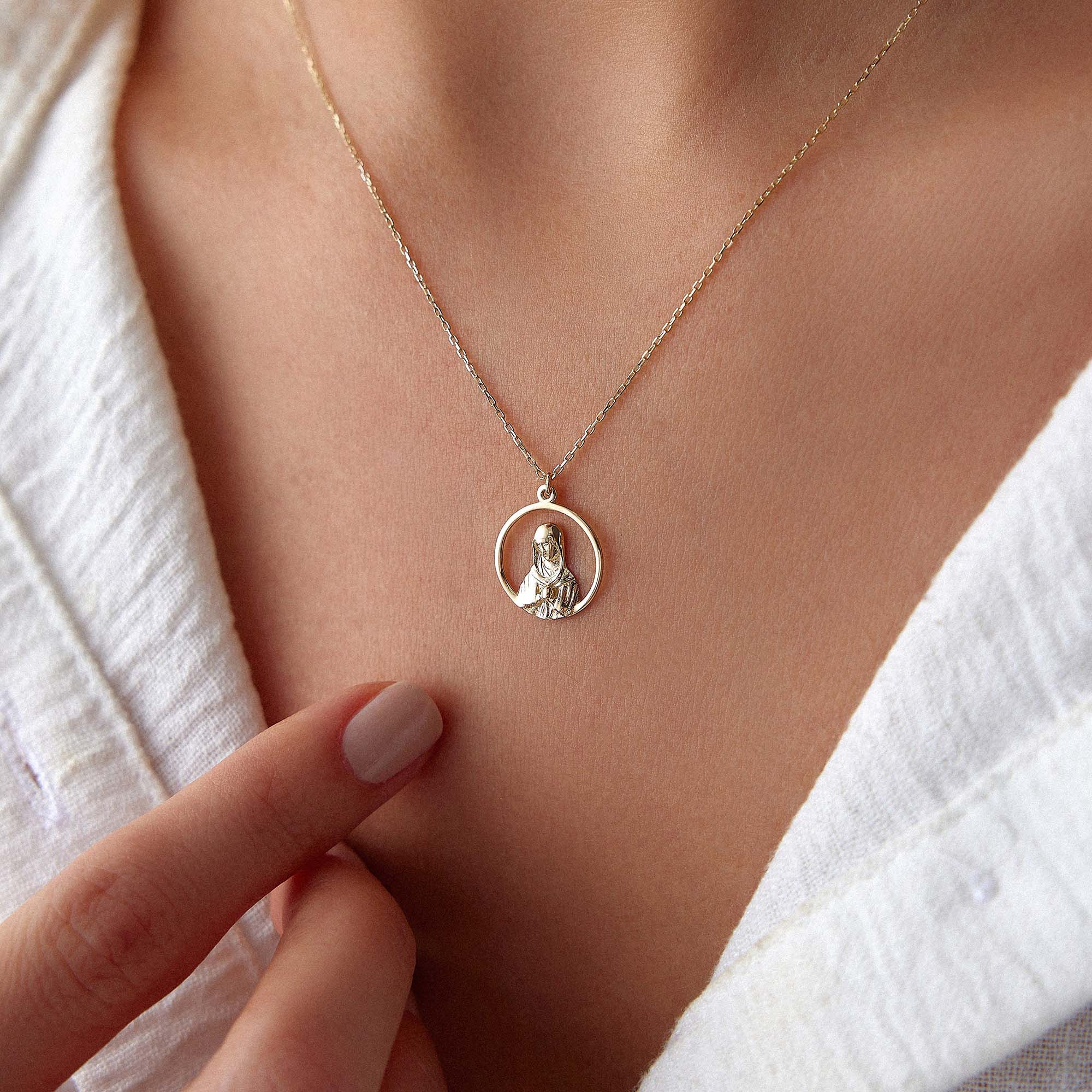 An upclose image of a model wearing an open virgin mary necklace