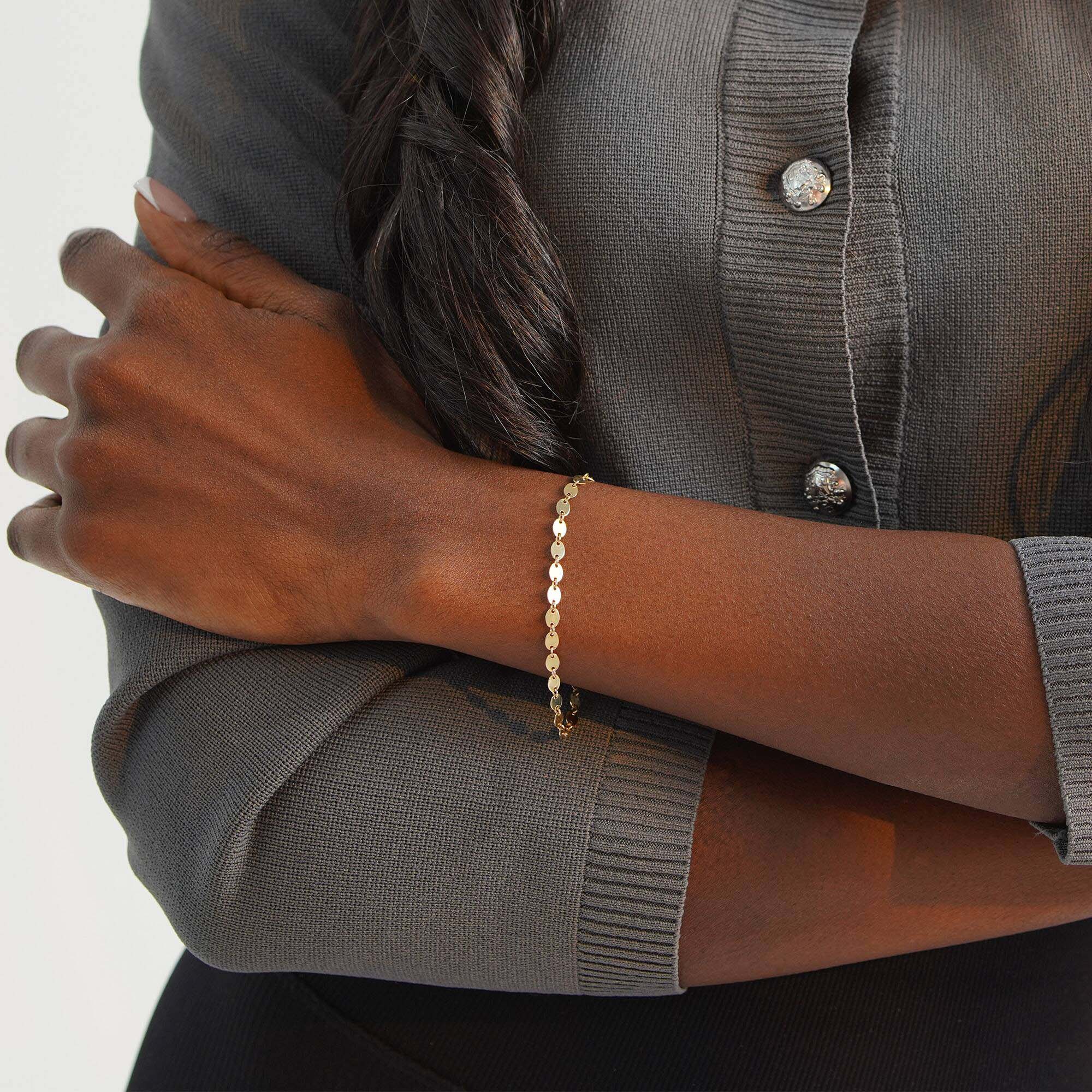 Person wearing a gold bracelet with a neutral background