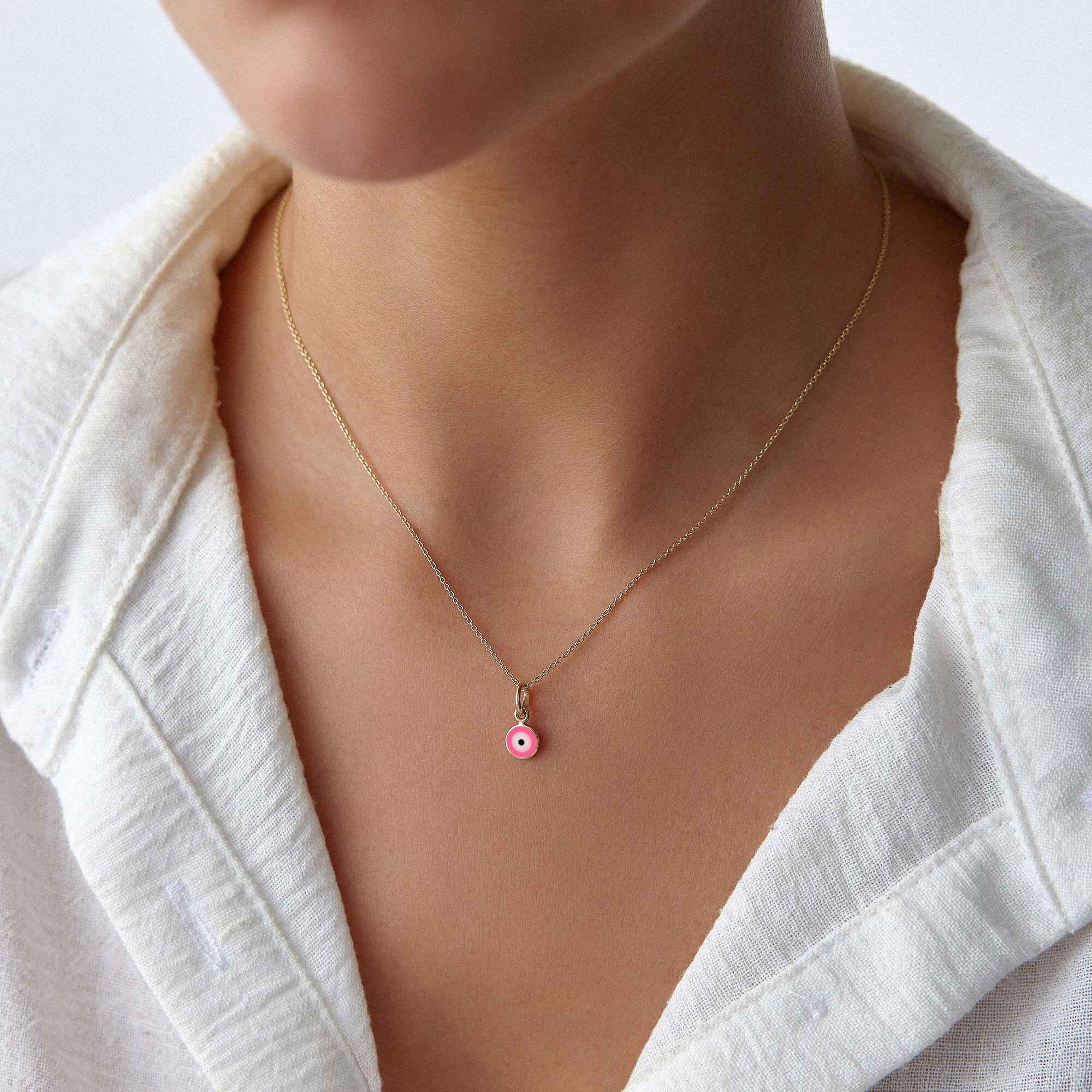 A model wearing a minimal pink evil eye pendant on a thin gold chain.