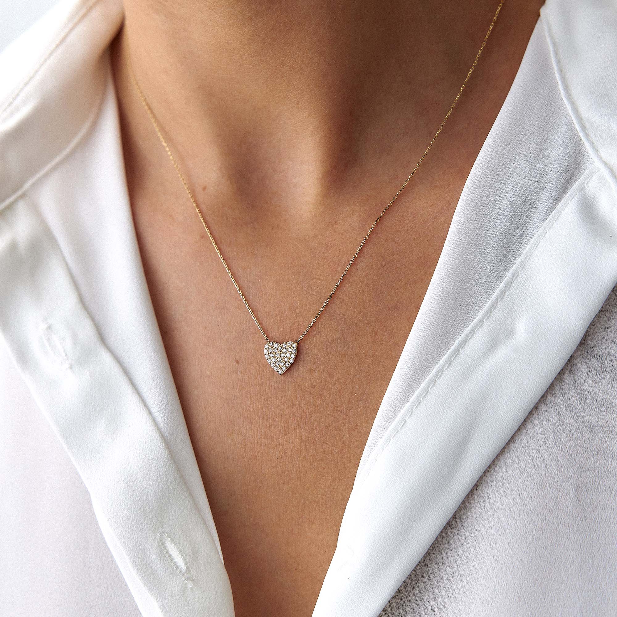 A minimal pave set heart-shaped necklace worn by a person in a white shirt