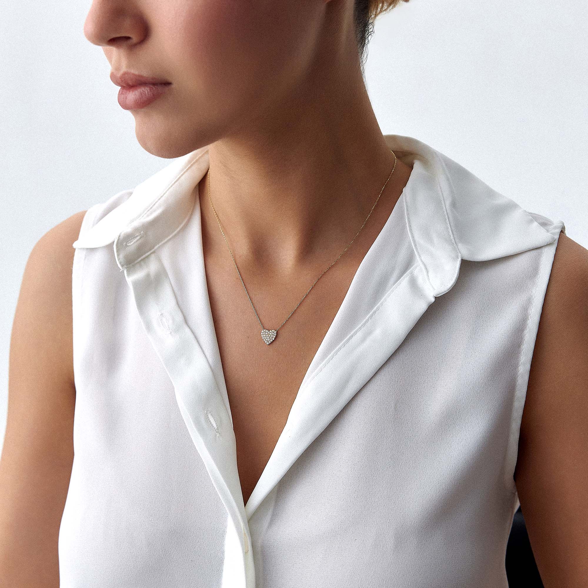 A minimal pave set heart-shaped necklace worn by a person in a white shirt