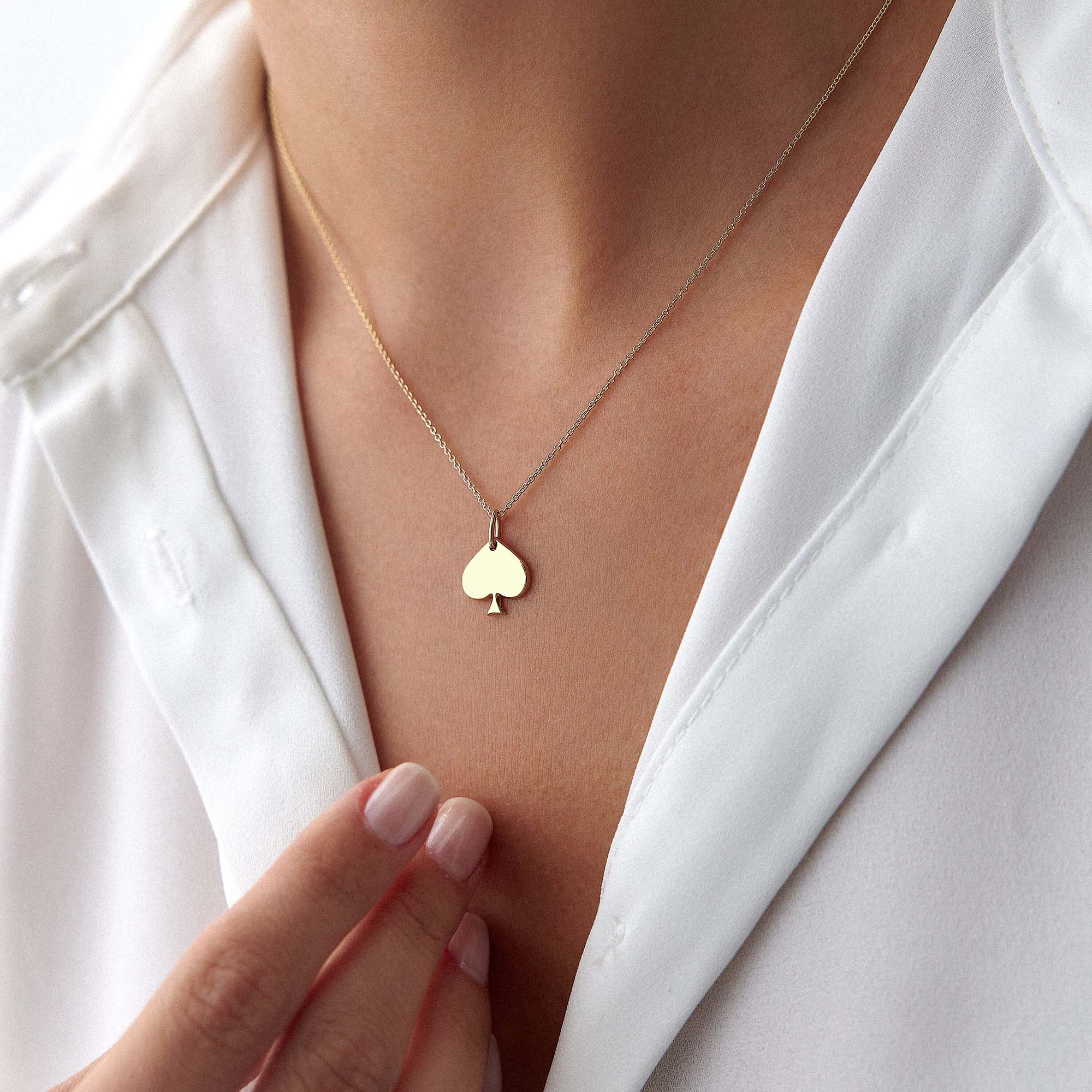 Gold necklace with a spade-shaped pendant worn by a person in a white shirt.