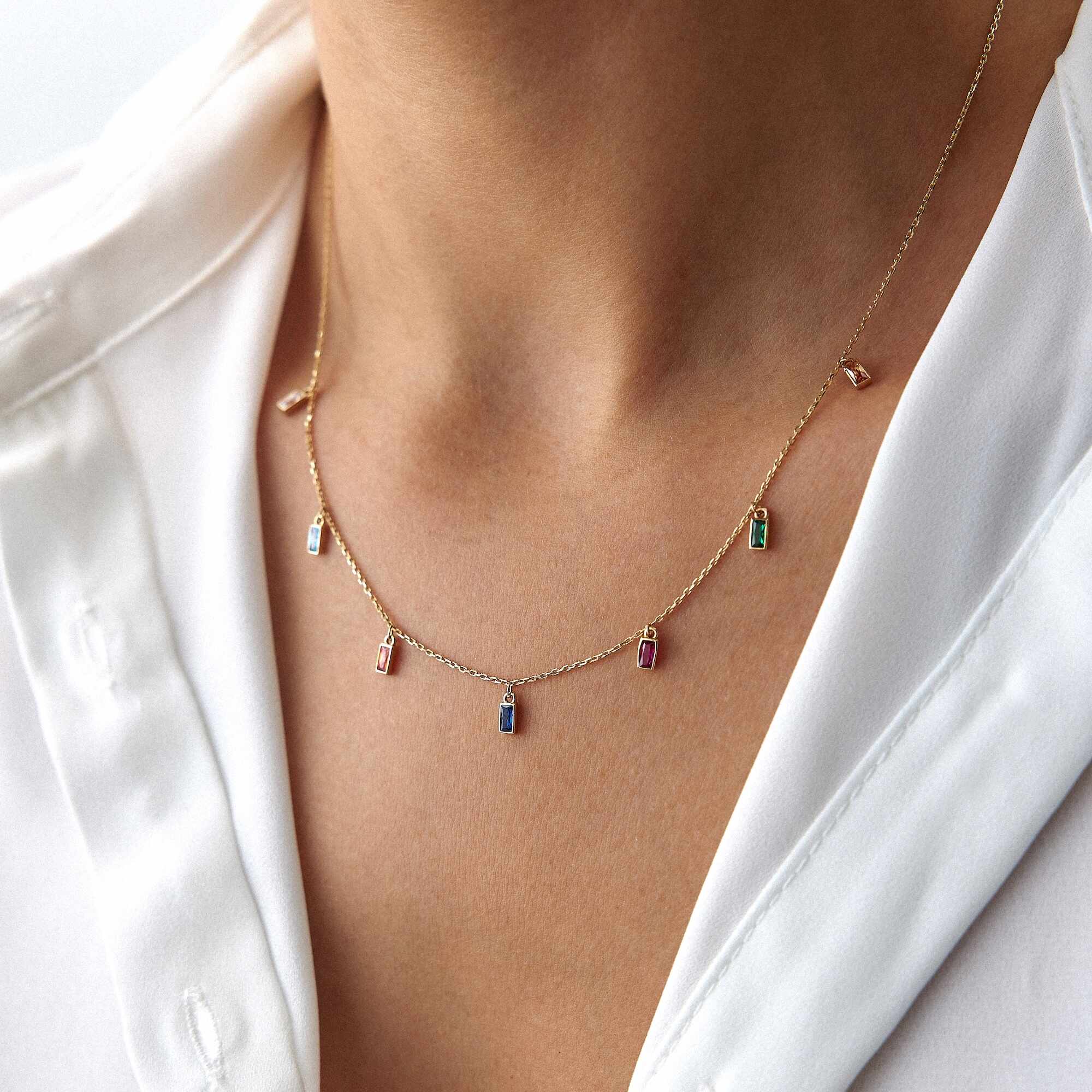 Necklace with small colorful pendants worn by a person in a white shirt.