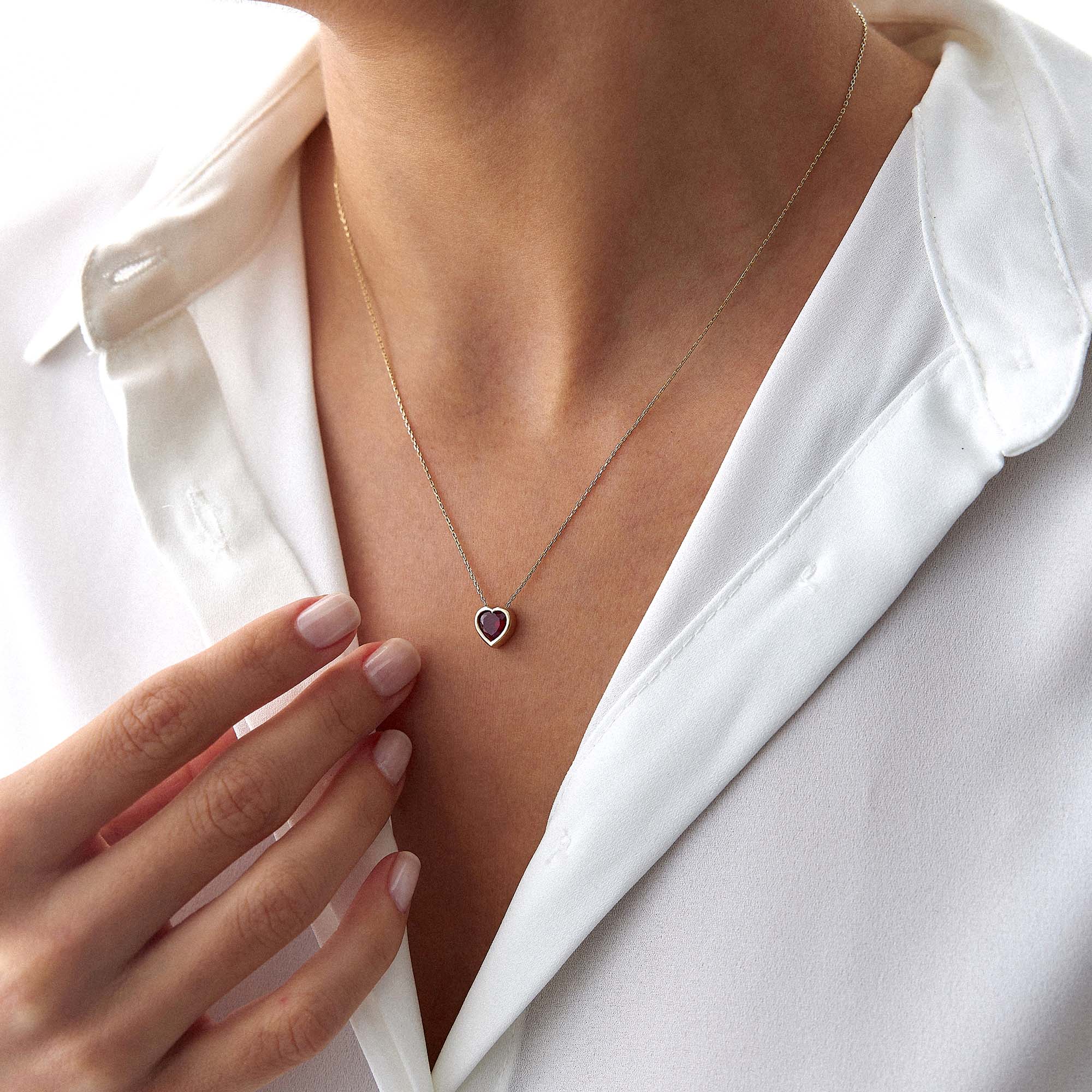 Necklace with a heart-shaped pendant worn by a person in a white shirt.