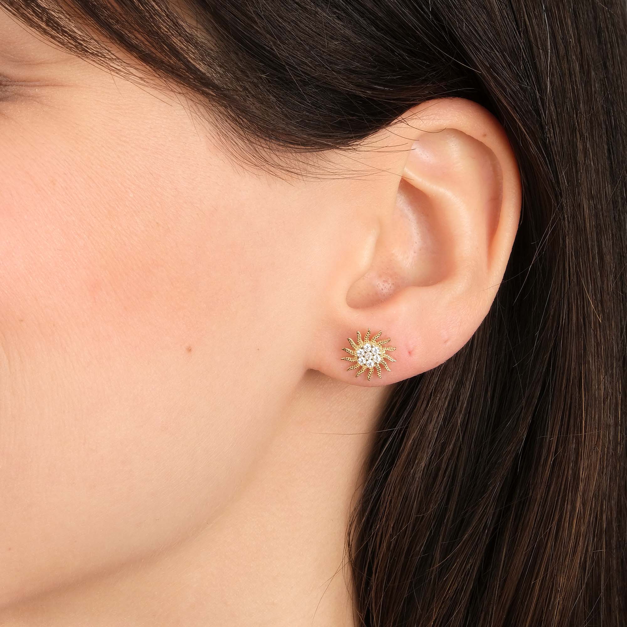 Close-up of an ear wearing a gold sun shaped earring.