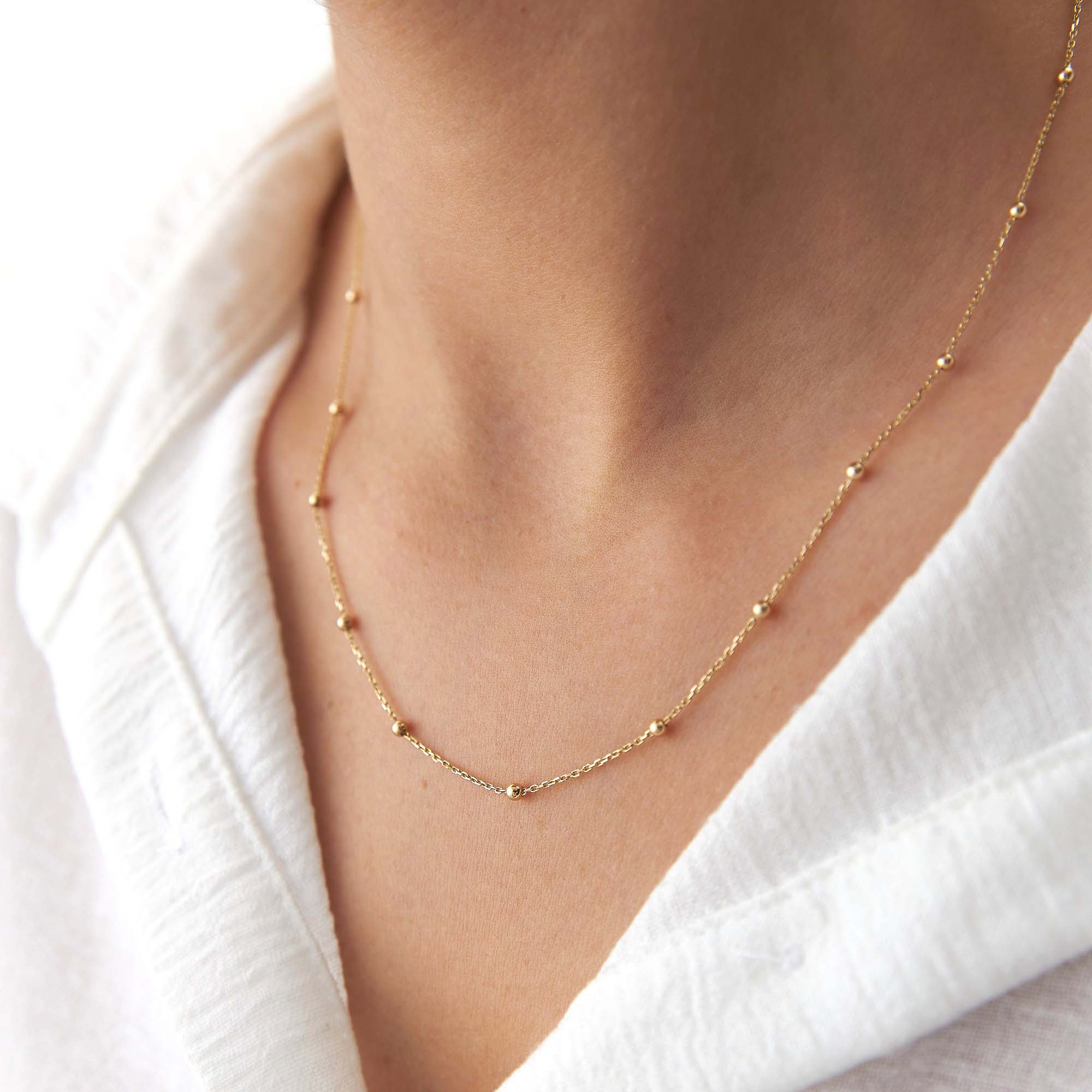 A 14k yellow gold satellite chain necklace on a model.