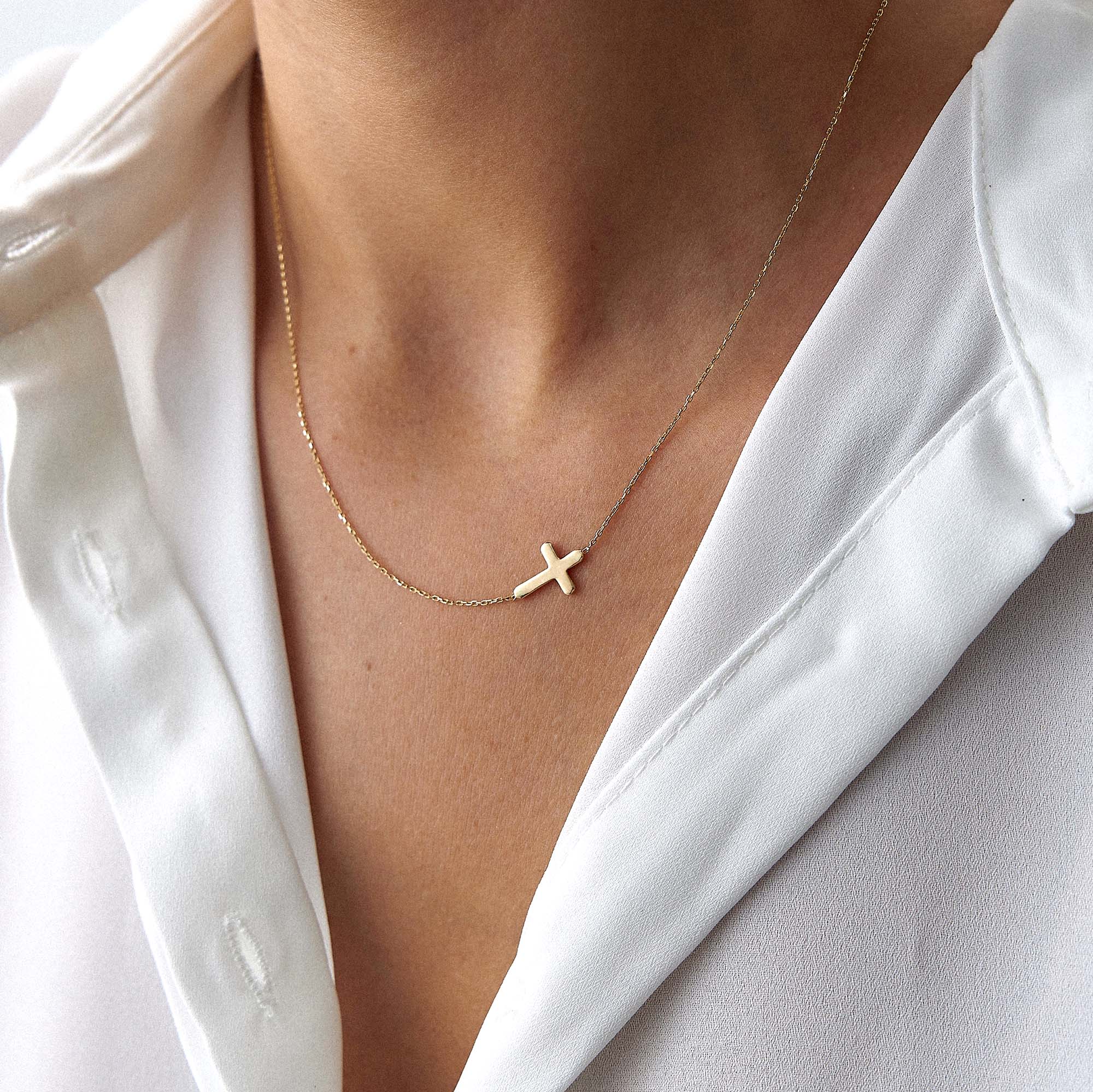 Gold necklace with a sideways cross pendant on a person wearing a white top.