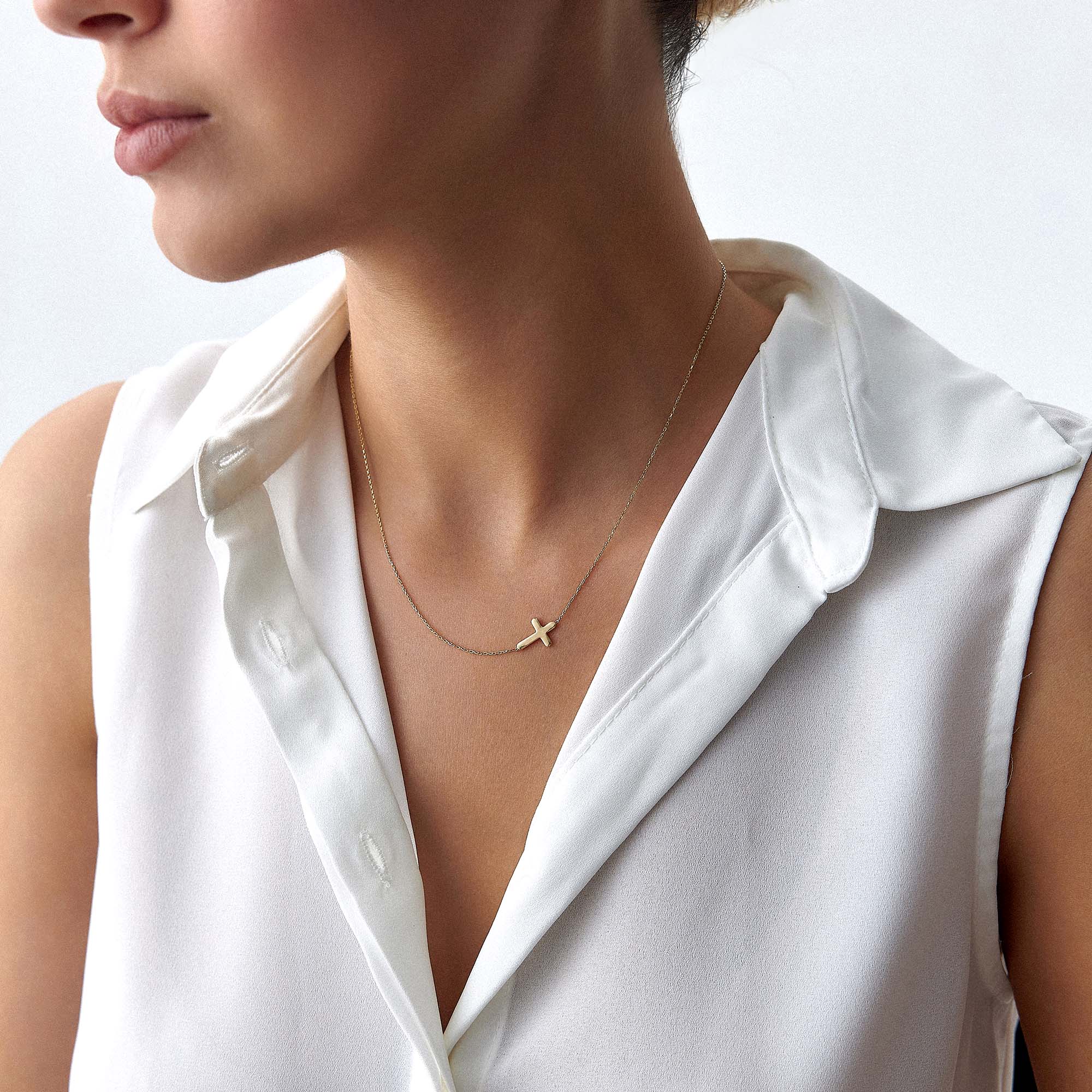 Gold necklace with a sideways cross pendant on a person wearing a white top.