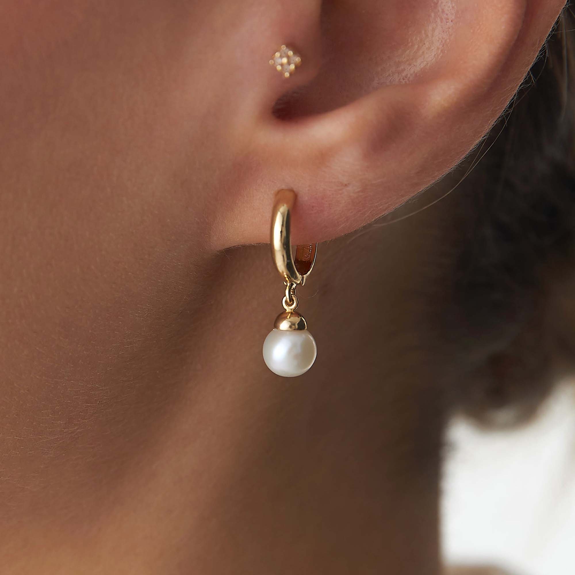 Gold hoop earring with a pearl drop worn by a person.