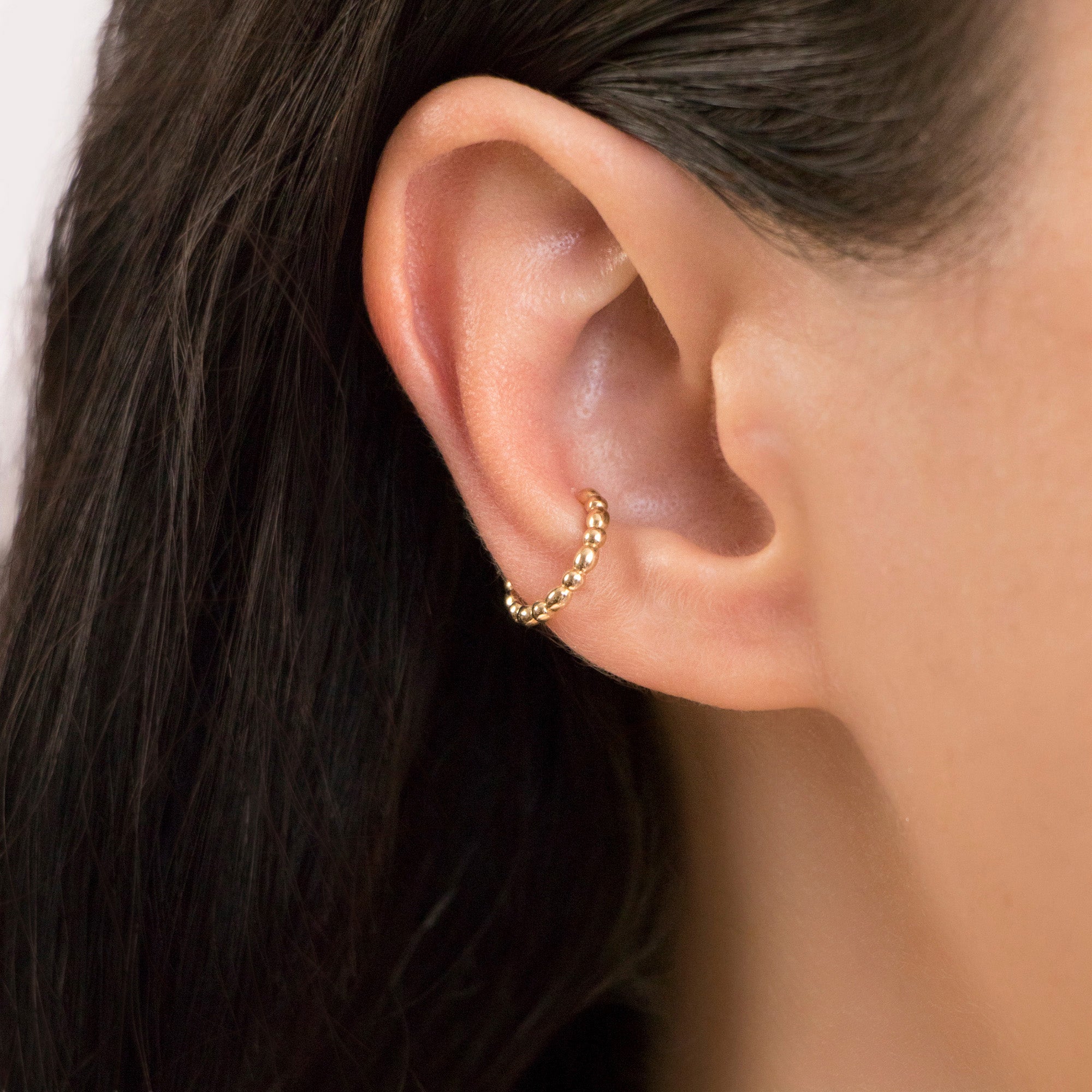 A person wearing a single gold beaded ear cuff on their ear.