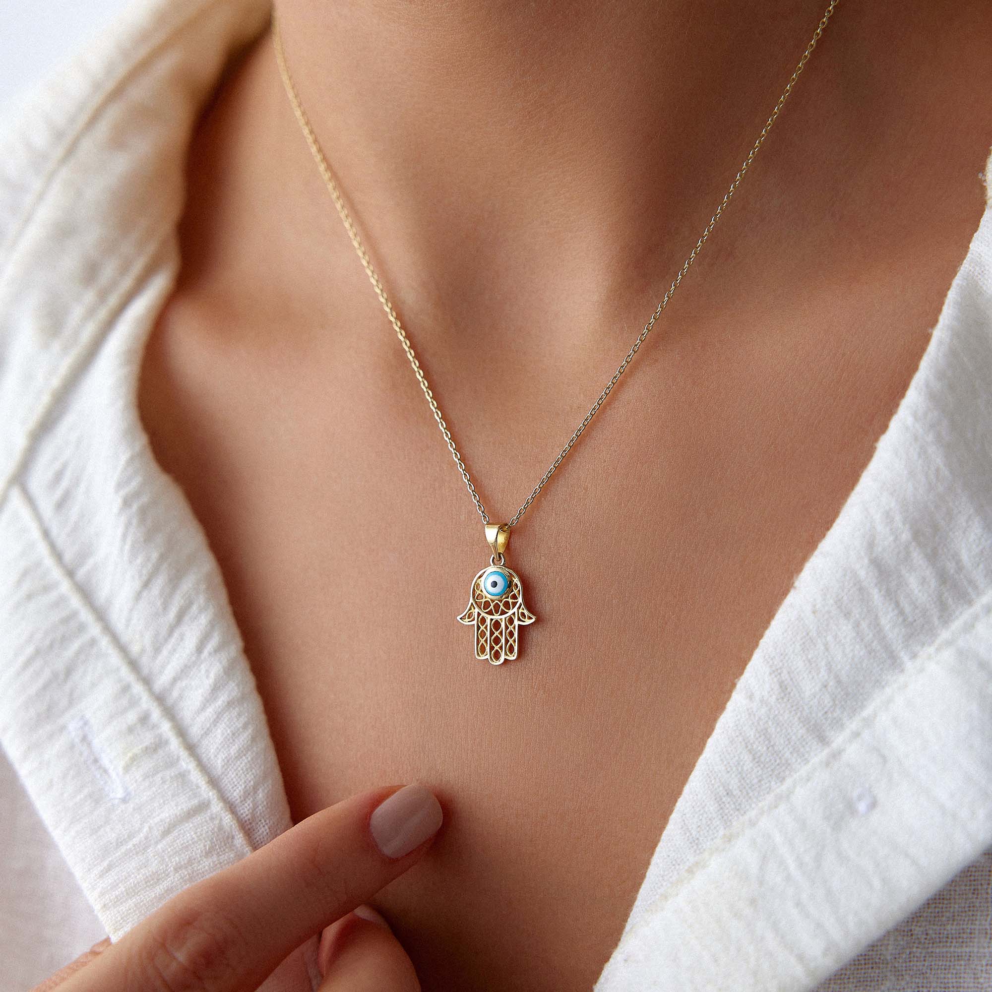 A model wearing a traditional small hamsa pendant with a blue evil eye center on a gold chain.
