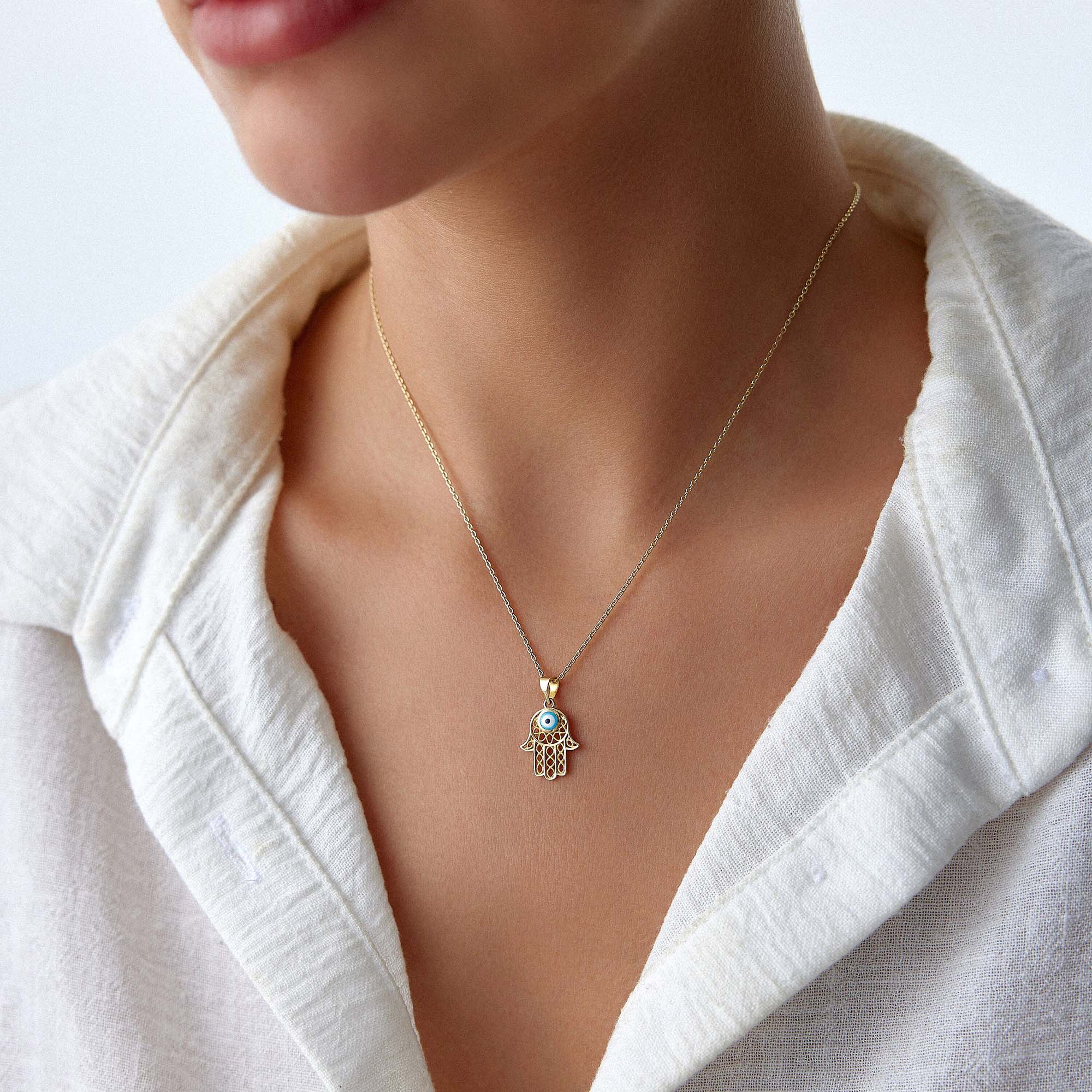 A model wearing a traditional small hamsa pendant with a blue evil eye center on a gold chain.