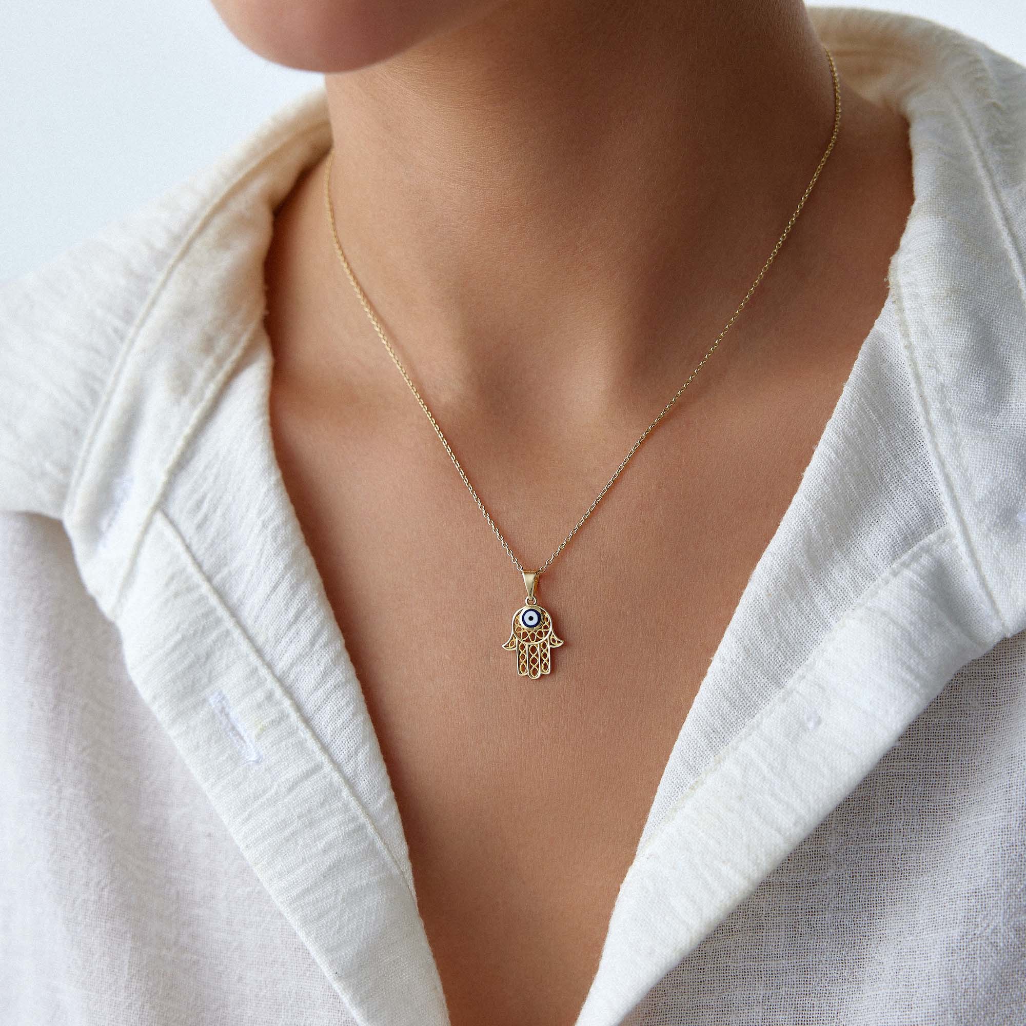 A model wearing a traditional small hamsa pendant with a navy blue evil eye center on a gold chain.