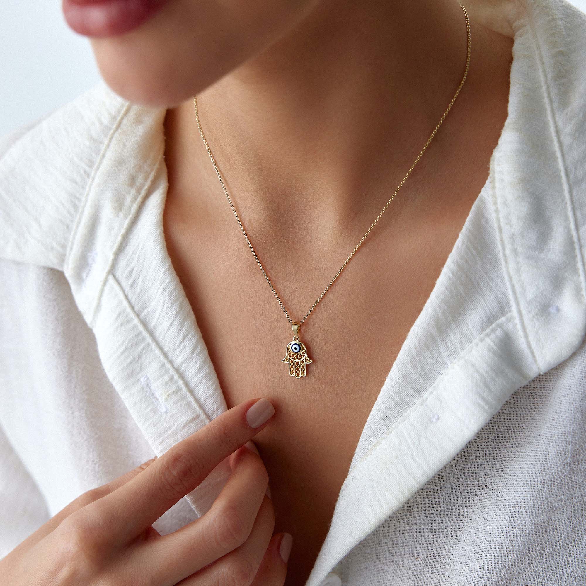 A model wearing a traditional small hamsa pendant with a navy blue evil eye center on a gold chain.