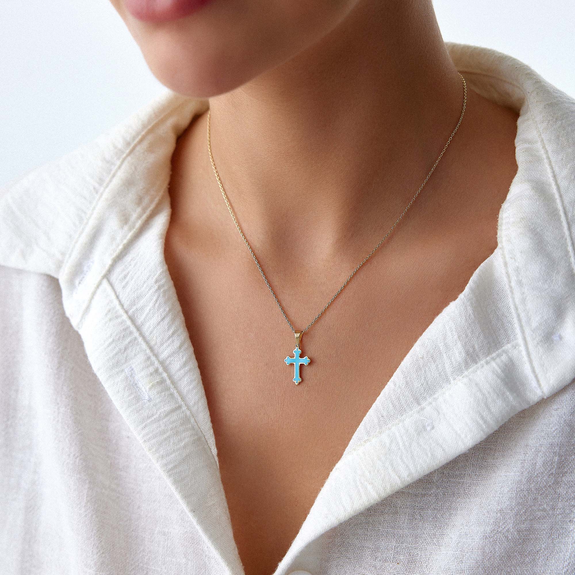 A model wearing a small ocean blue cross pendant on a thin gold chain