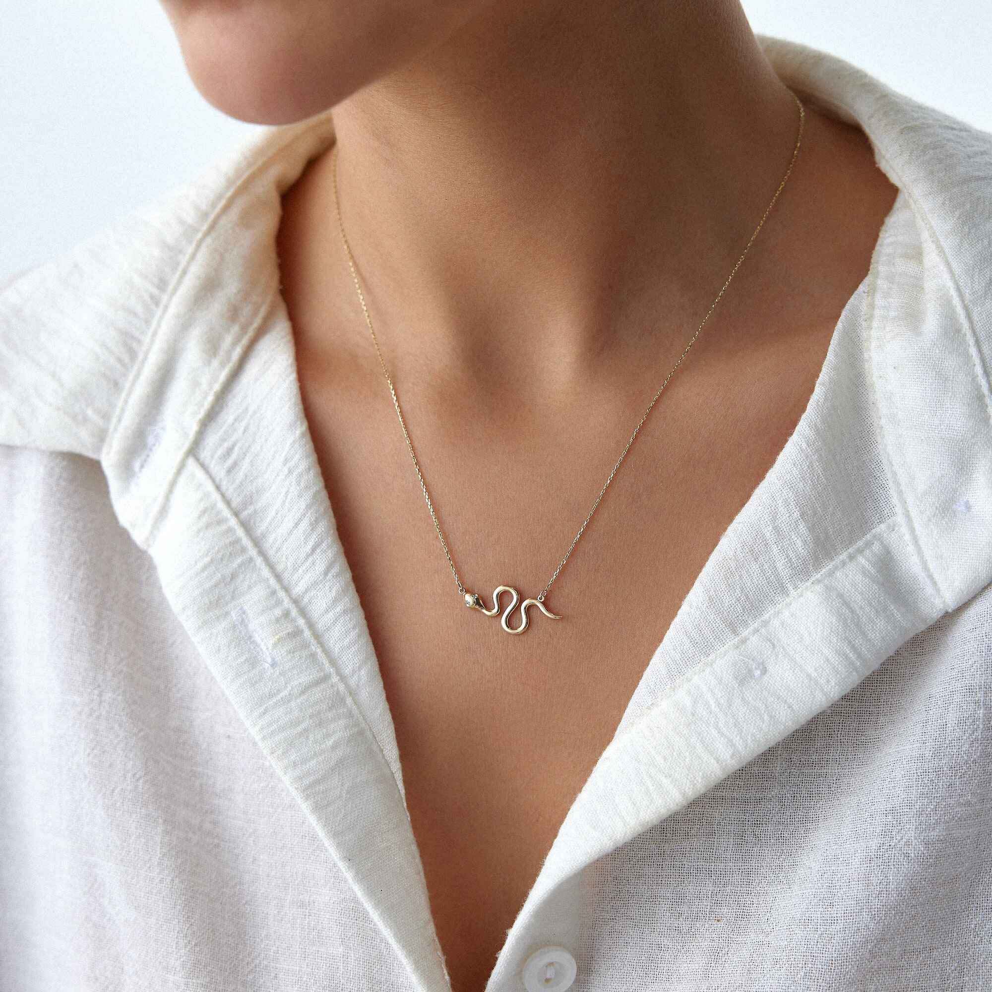 Gold snake necklace worn by a person in a white shirt