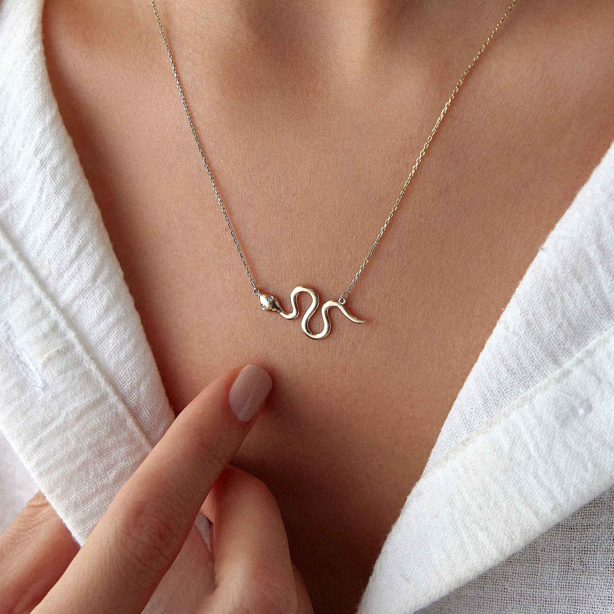 Gold snake necklace on a person wearing a white garment