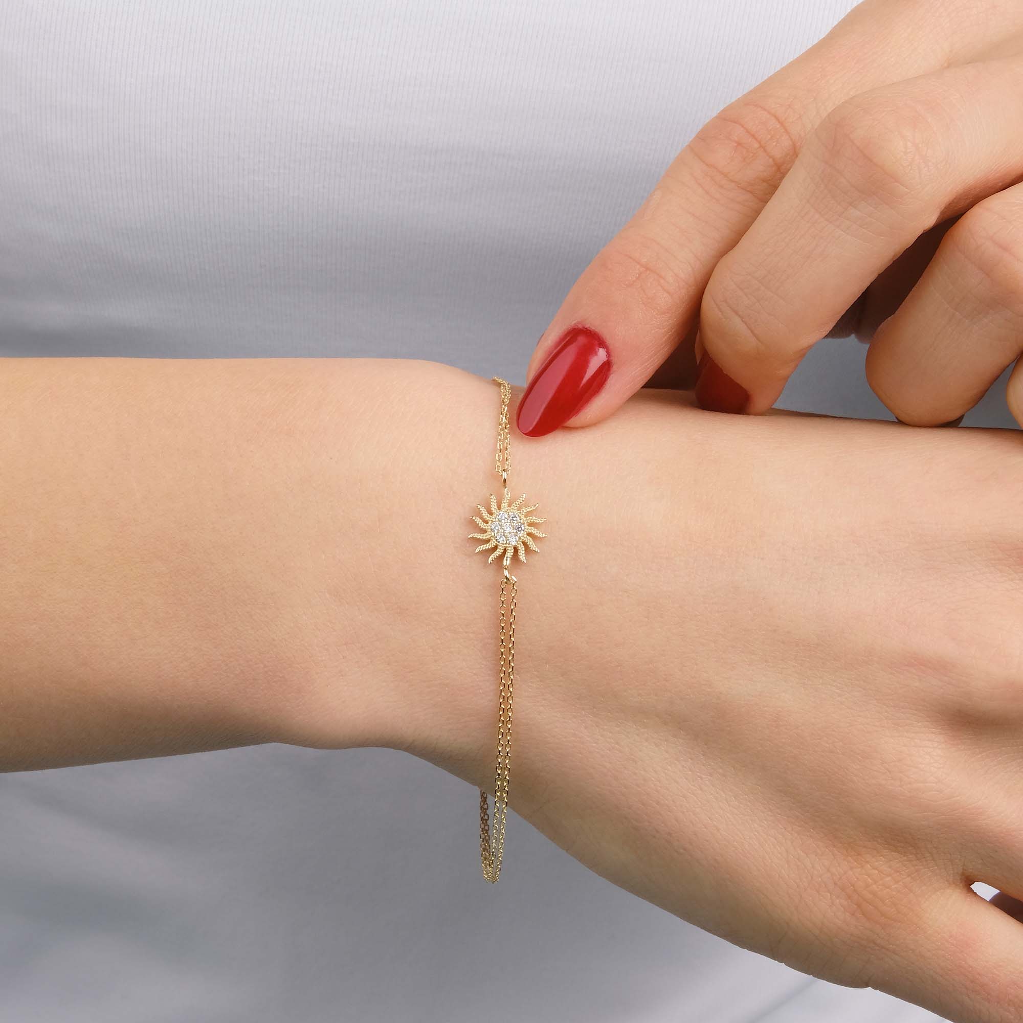 Gold bracelet with a sun design on a wrist against a neutral background