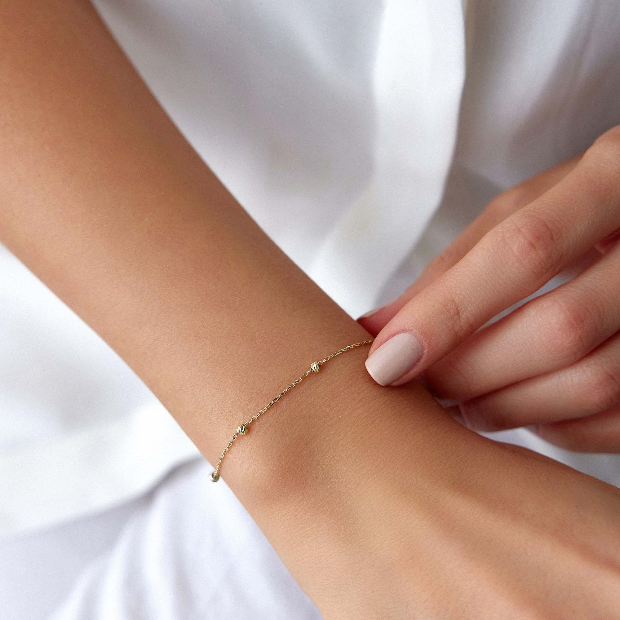 A delicate gold bracelet with small beads strung on a chain, fastened with a gold clasp.
