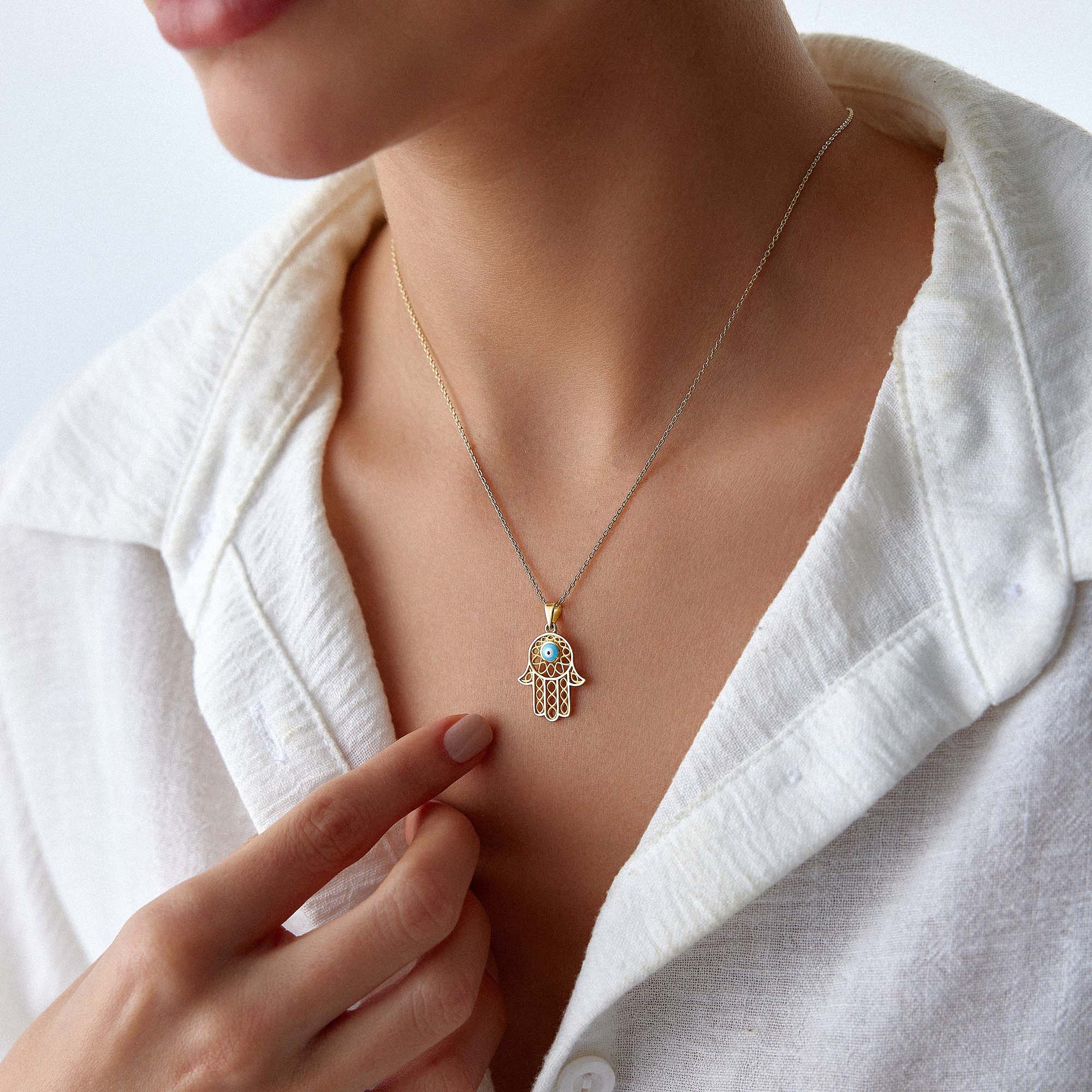 A model wearing a traditional large hamsa pendant with a blue evil eye center on a gold chain.