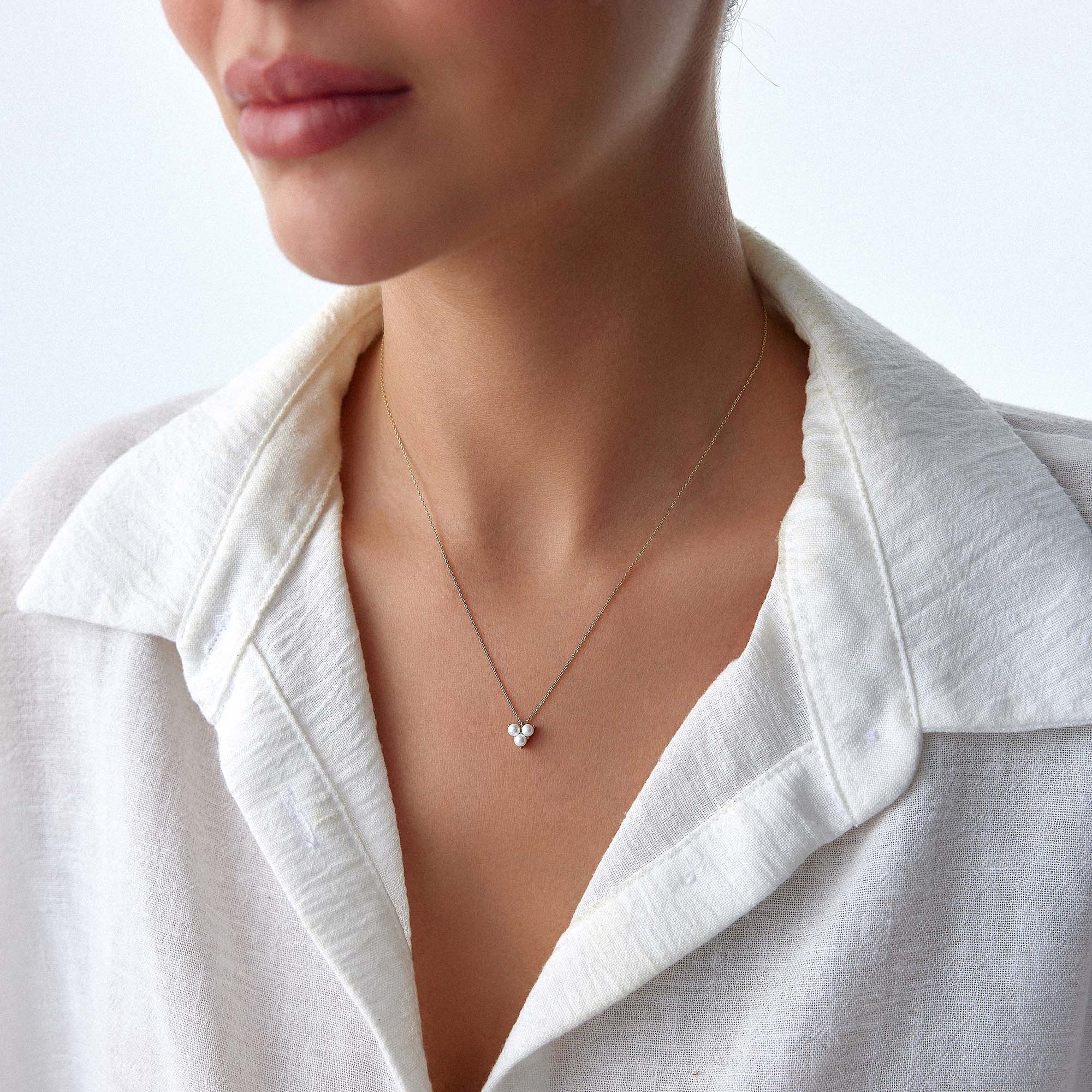 Close-up of a person wearing a delicate pearl necklace with a white shirt on a light background