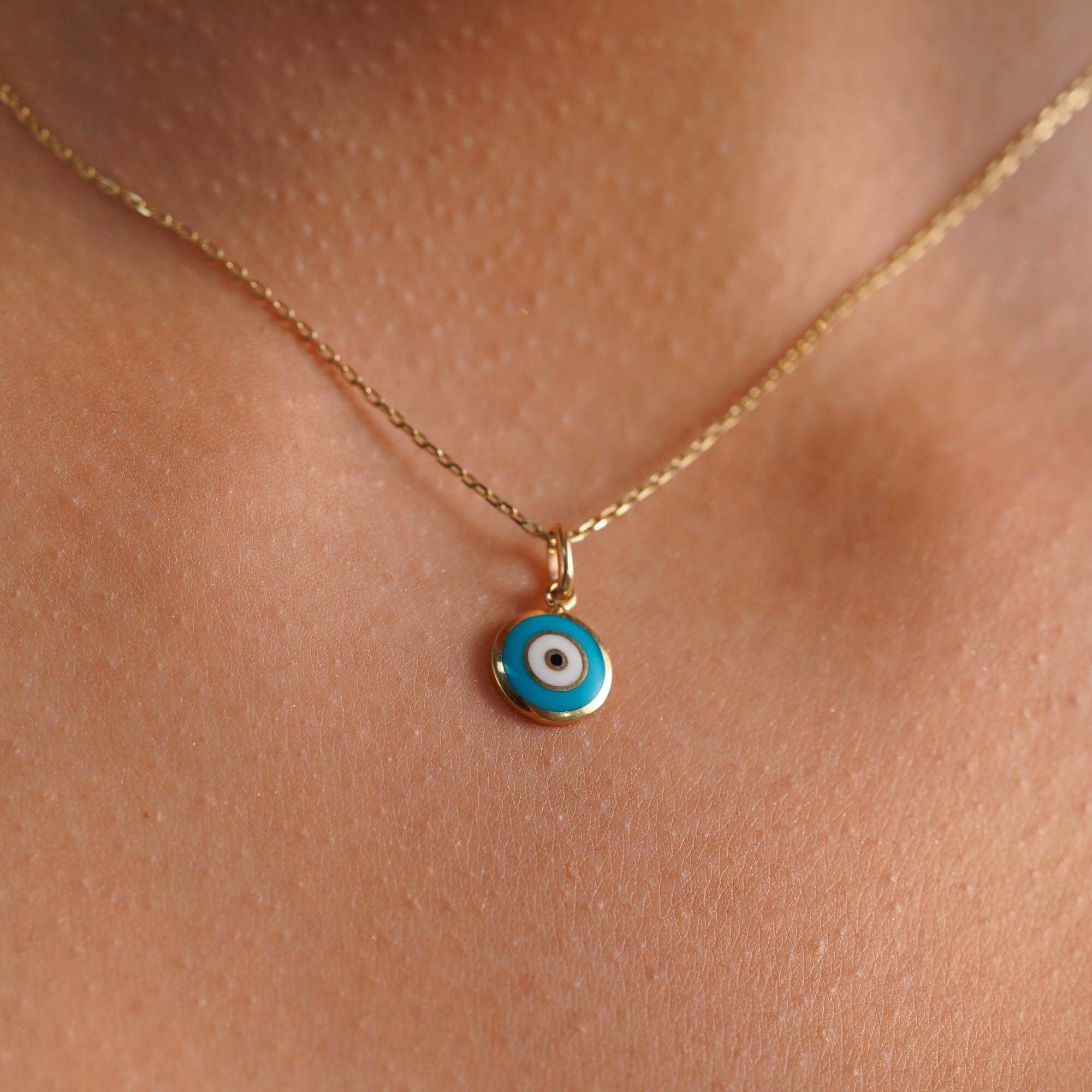 A model wearing a turquoise blue evil eye pendant on a gold chain.