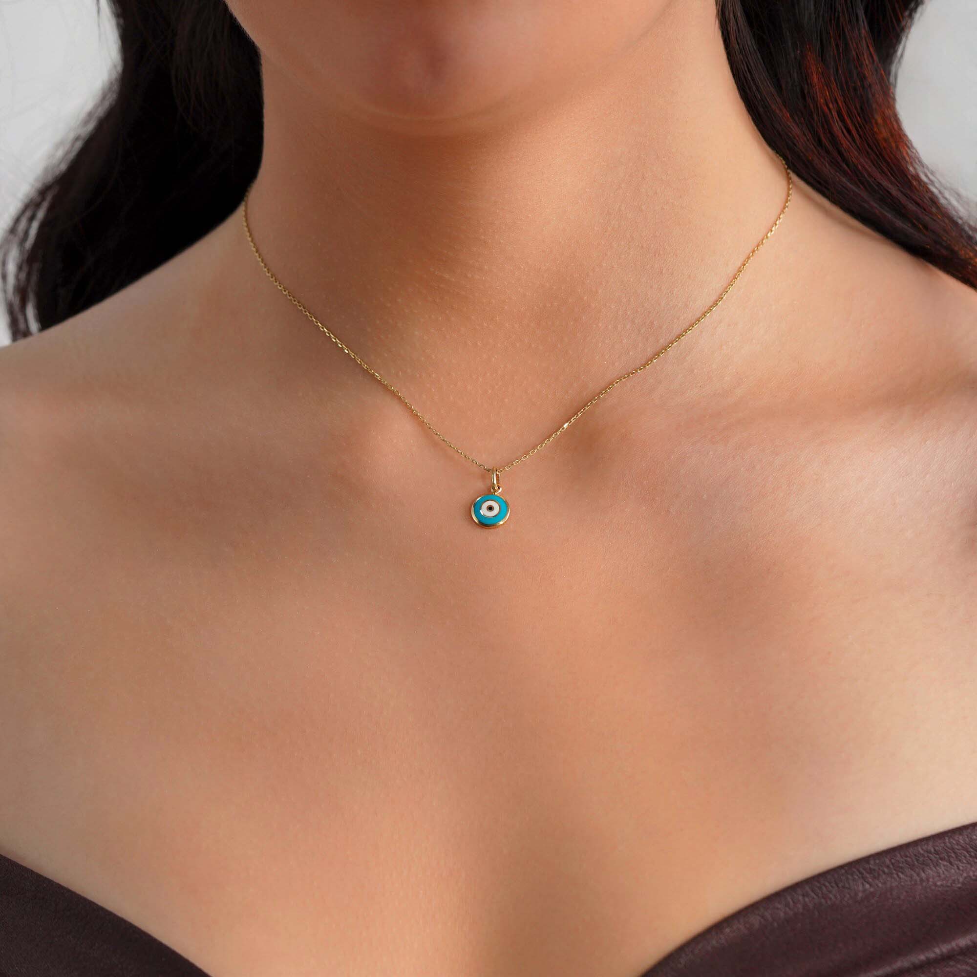 A model wearing a turquoise blue evil eye pendant on a gold chain.