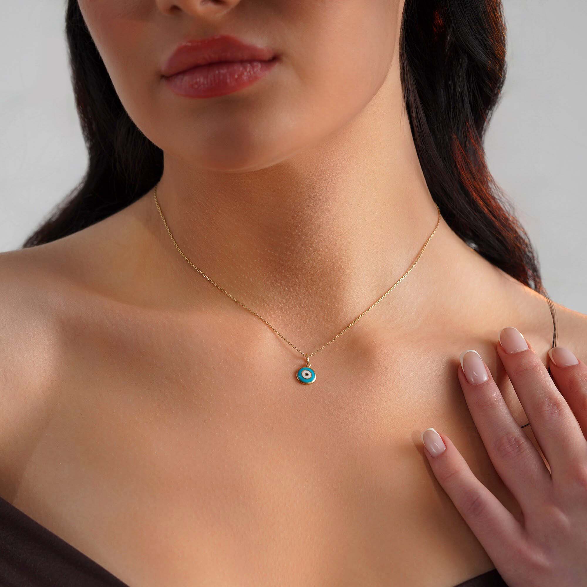 A model wearing a turquoise blue evil eye pendant on a gold chain.