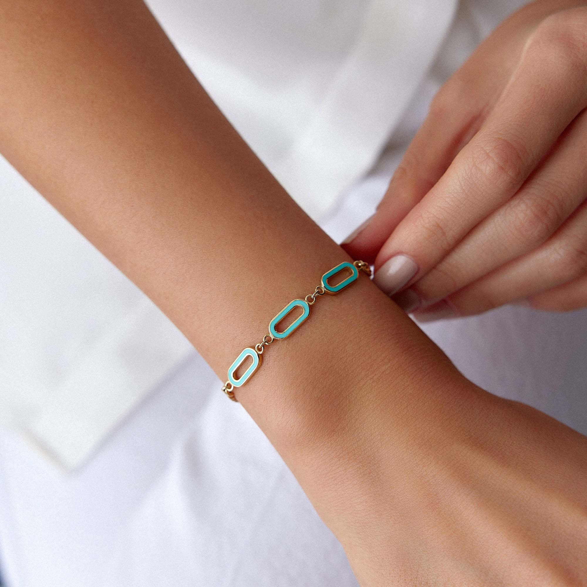 A 14K gold solid oval link chain bracelet with turquoise enamel accents on the central links, displayed on a wrist.