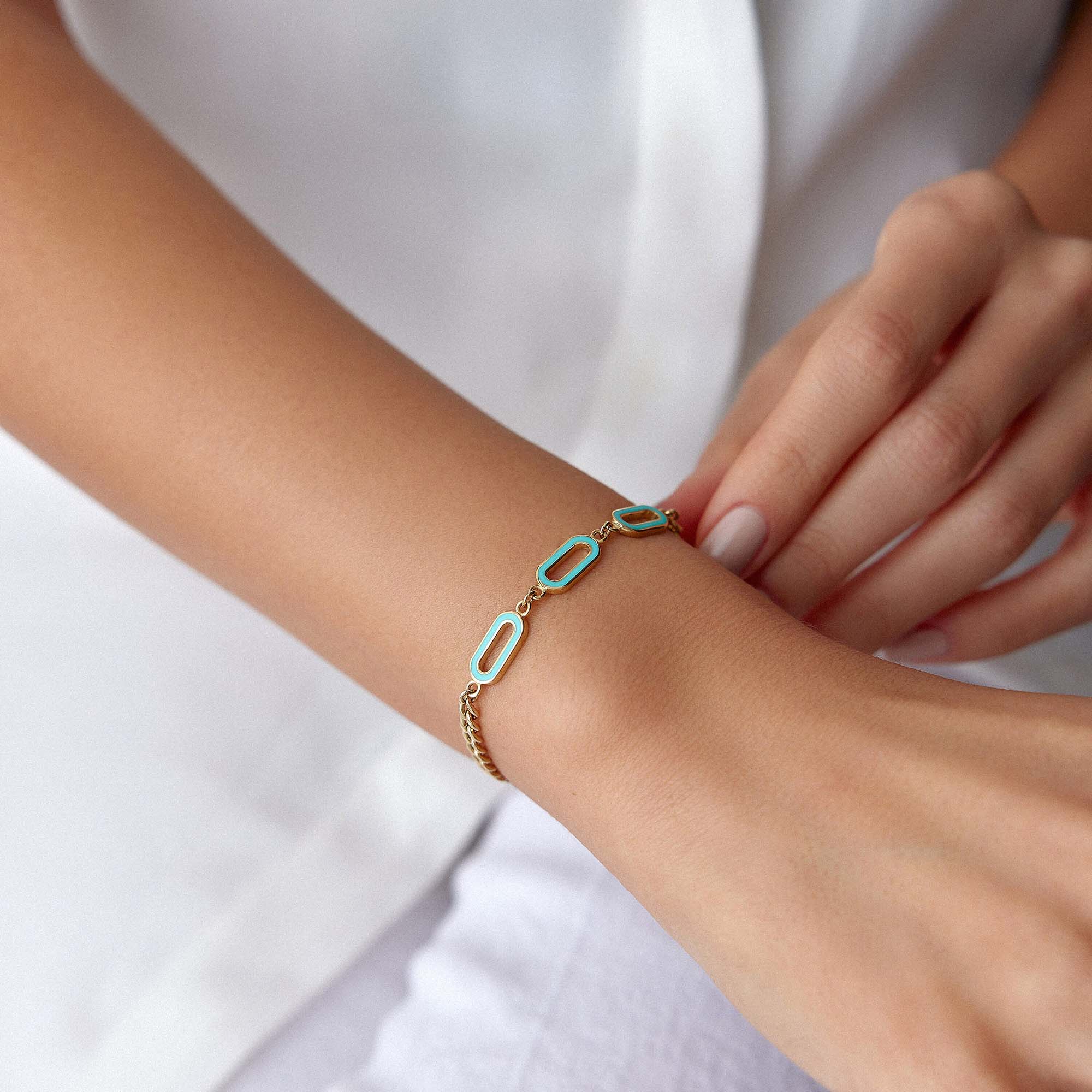 A 14K gold solid oval link chain bracelet with turquoise enamel accents on the central links, displayed on a wrist.